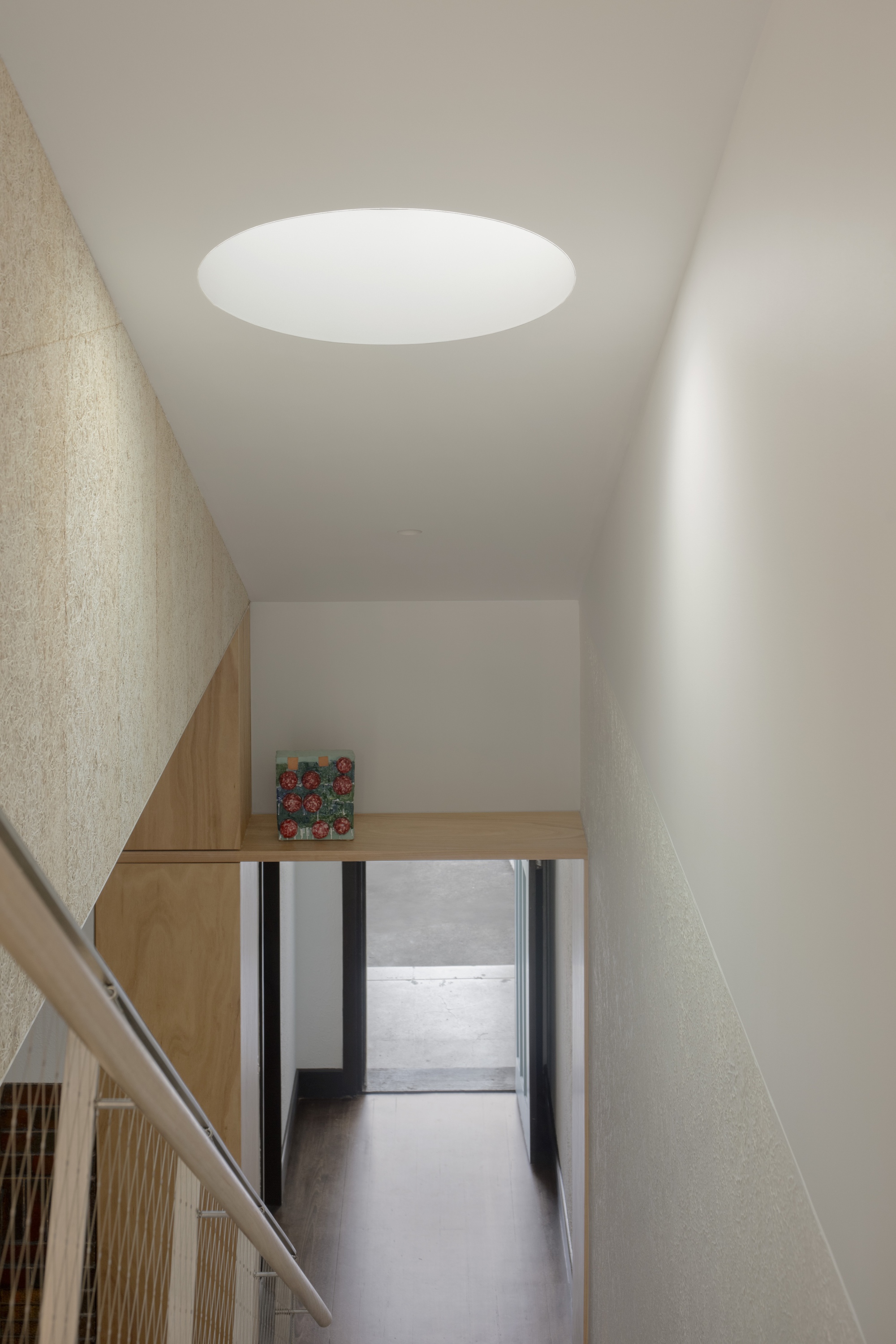 Upper level hallway with circular skylight above textured plaster walls and timber handrail