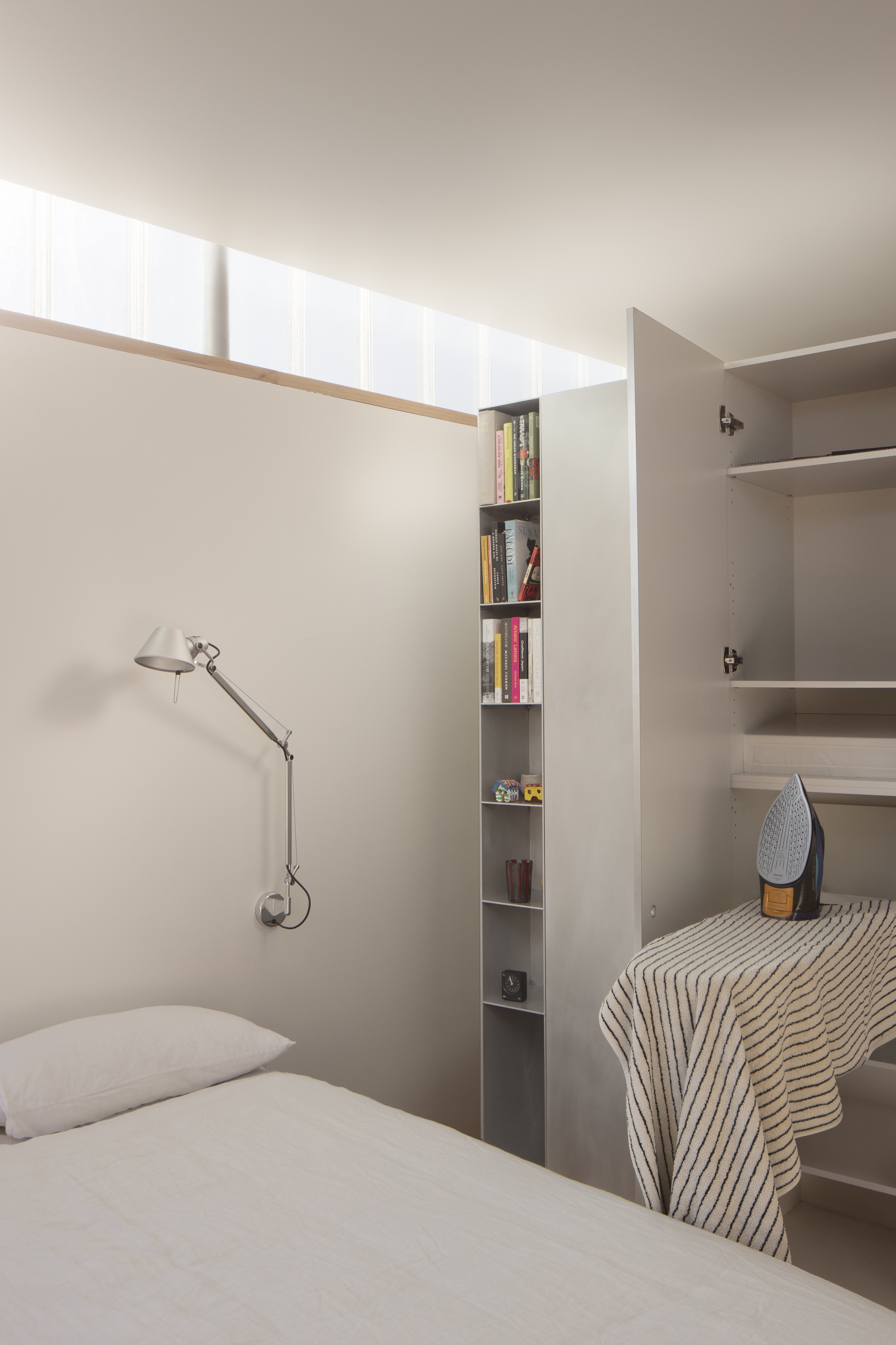 Bedroom with high clerestory windows above built-in bookshelf and articulated wall lamp