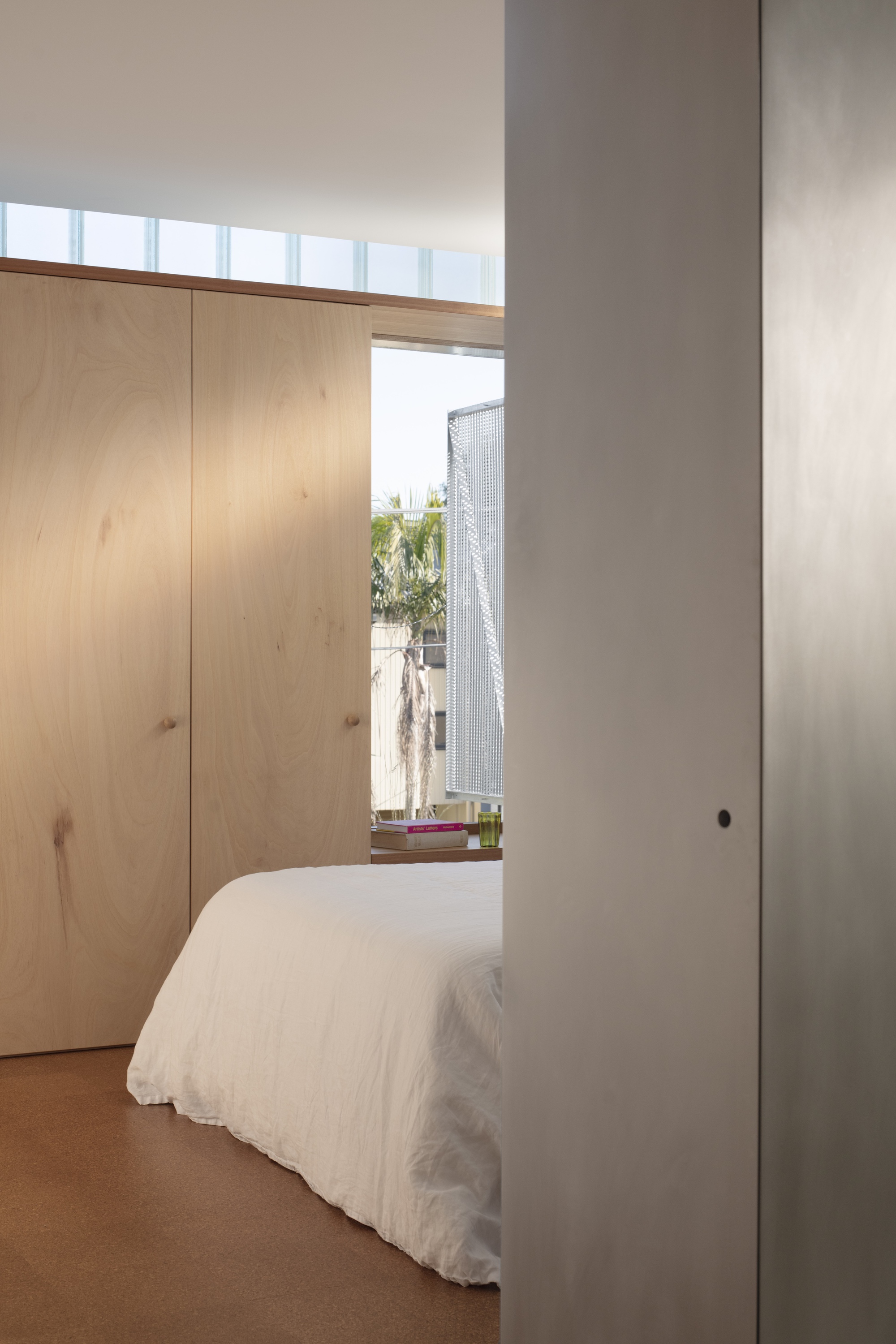 Bedroom view through plywood cabinetry toward window framing palm fronds outside