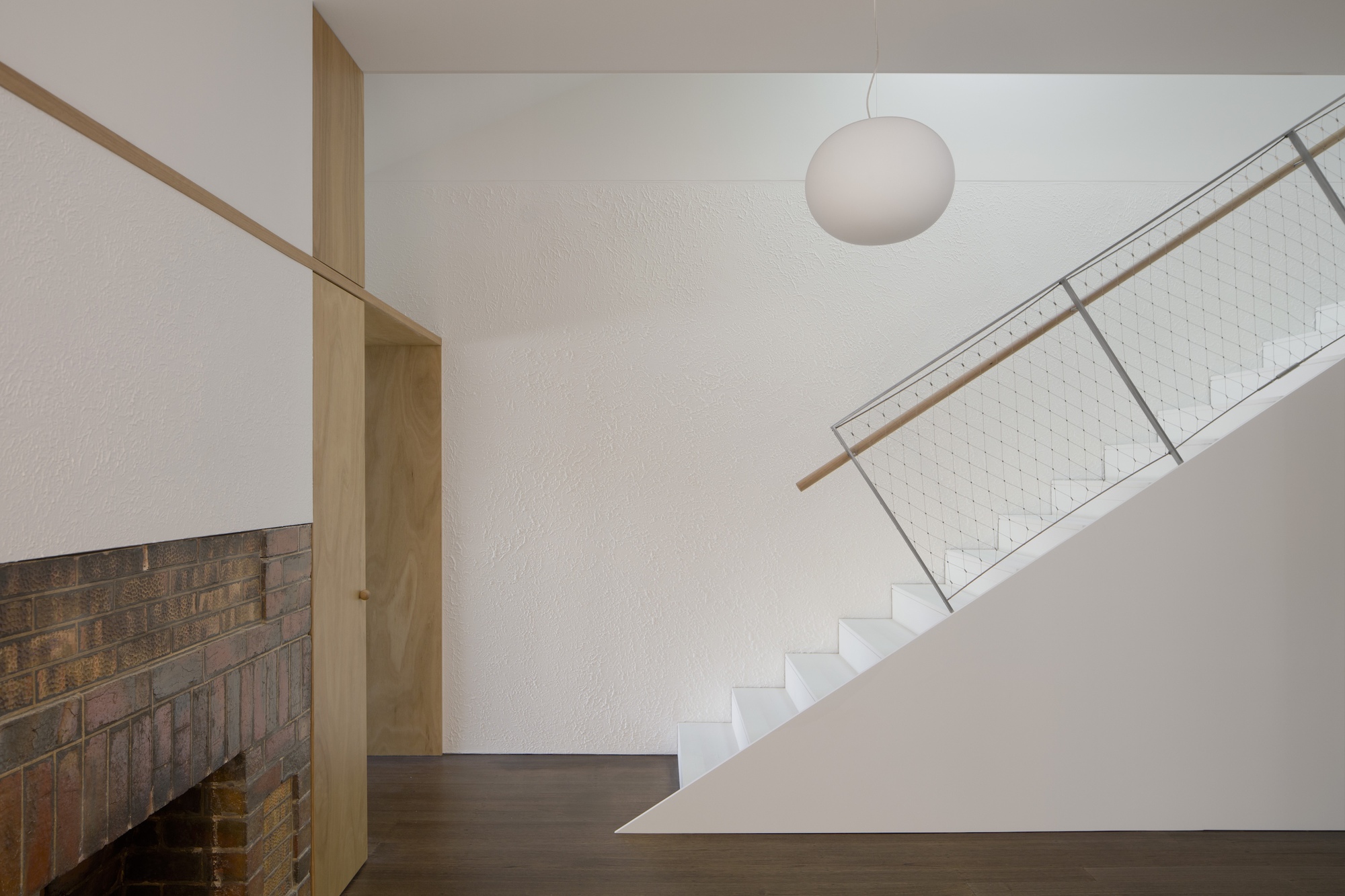 Staircase with timber handrail and wire mesh balustrade beside a textured brick wall