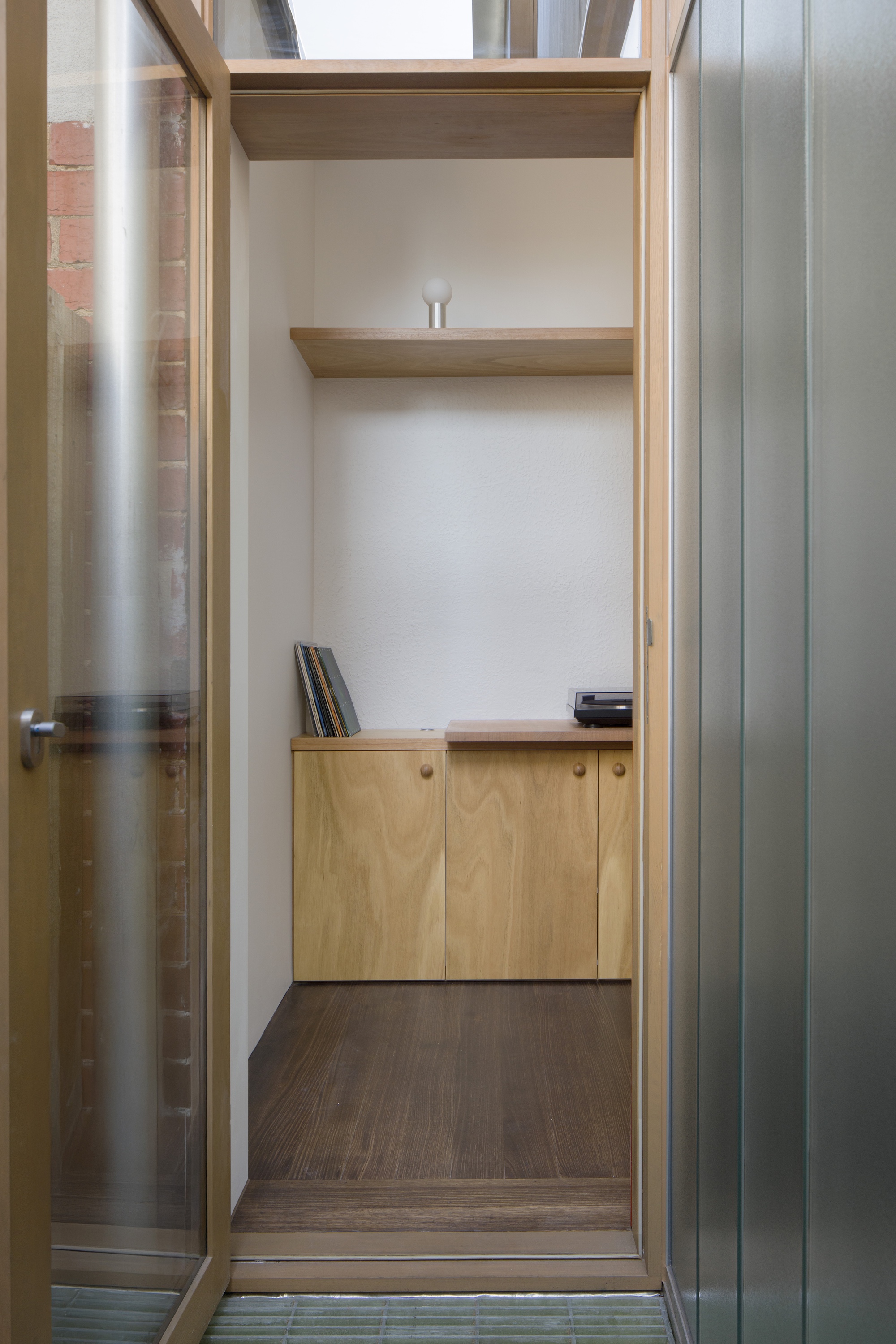 View through galvanized metal door frame into timber-lined alcove with built-in shelving and cabinets