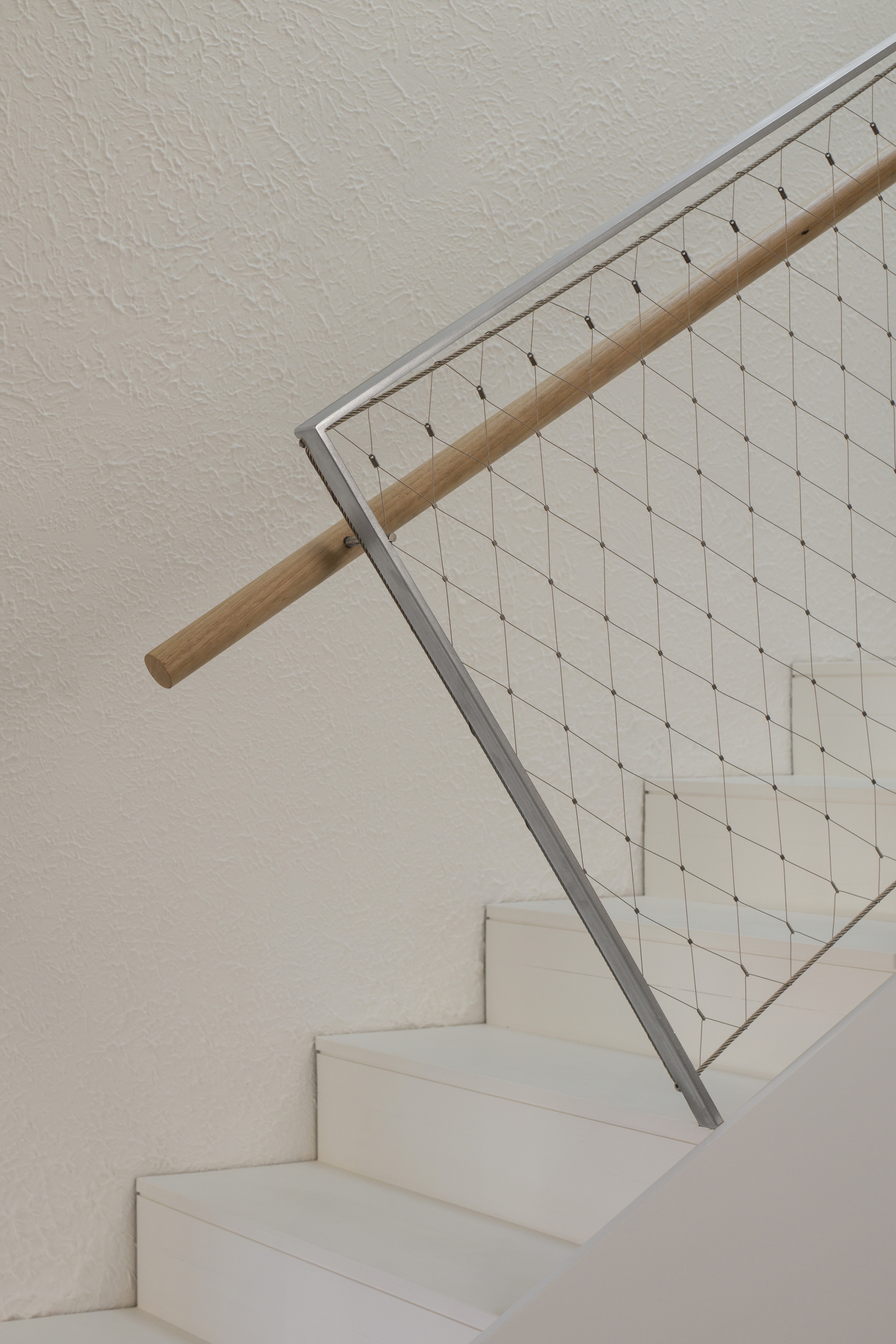 White stair with timber handrail and steel mesh balustrade against a textured plaster wall