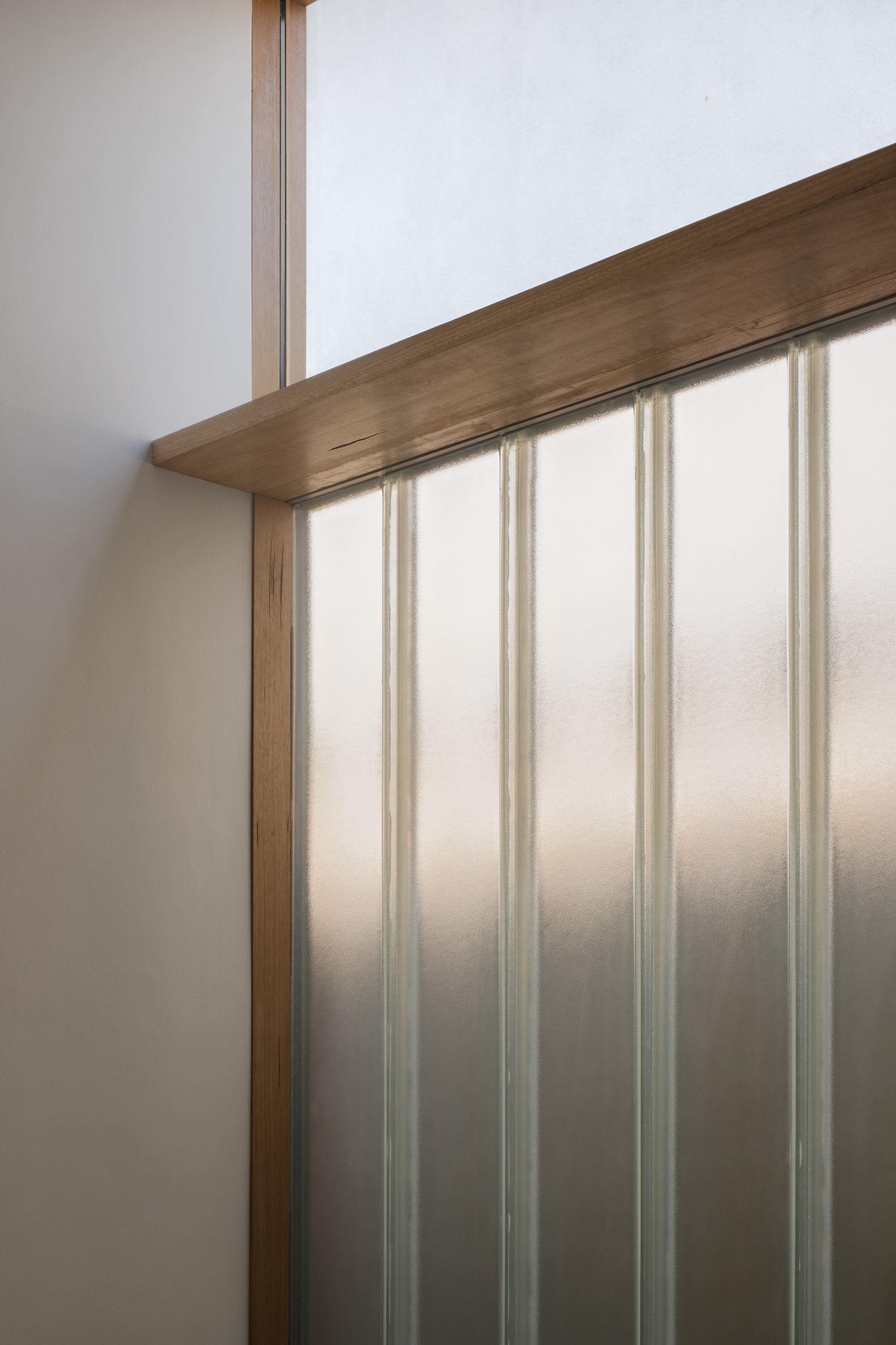 Close-up of timber handrail meeting translucent polycarbonate wall panel with vertical supports