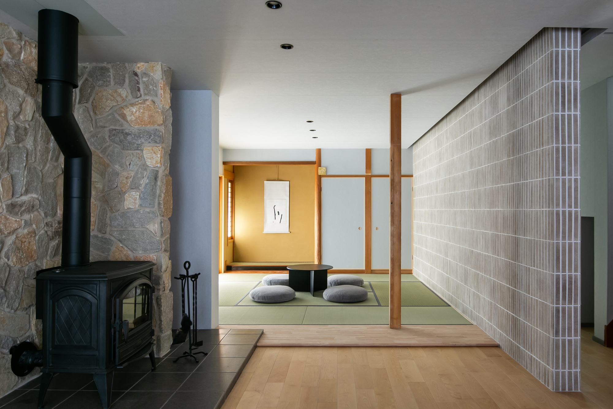 Black woodstove against a fieldstone wall beside a tatami room with vertical slatted screen