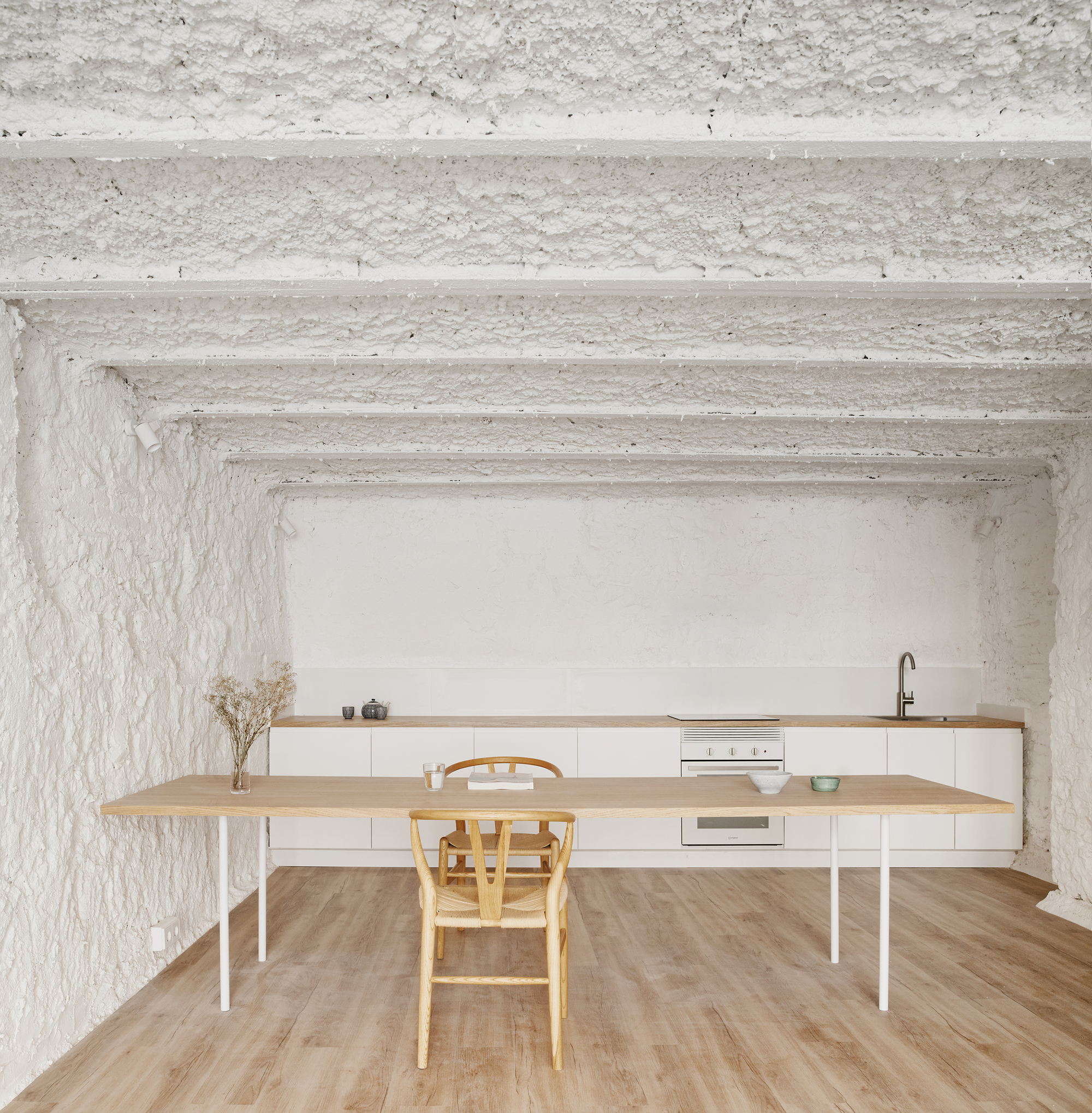 Kitchen with white base cabinets, timber countertop and dining table beneath whitewashed vaulted ceiling with exposed beams