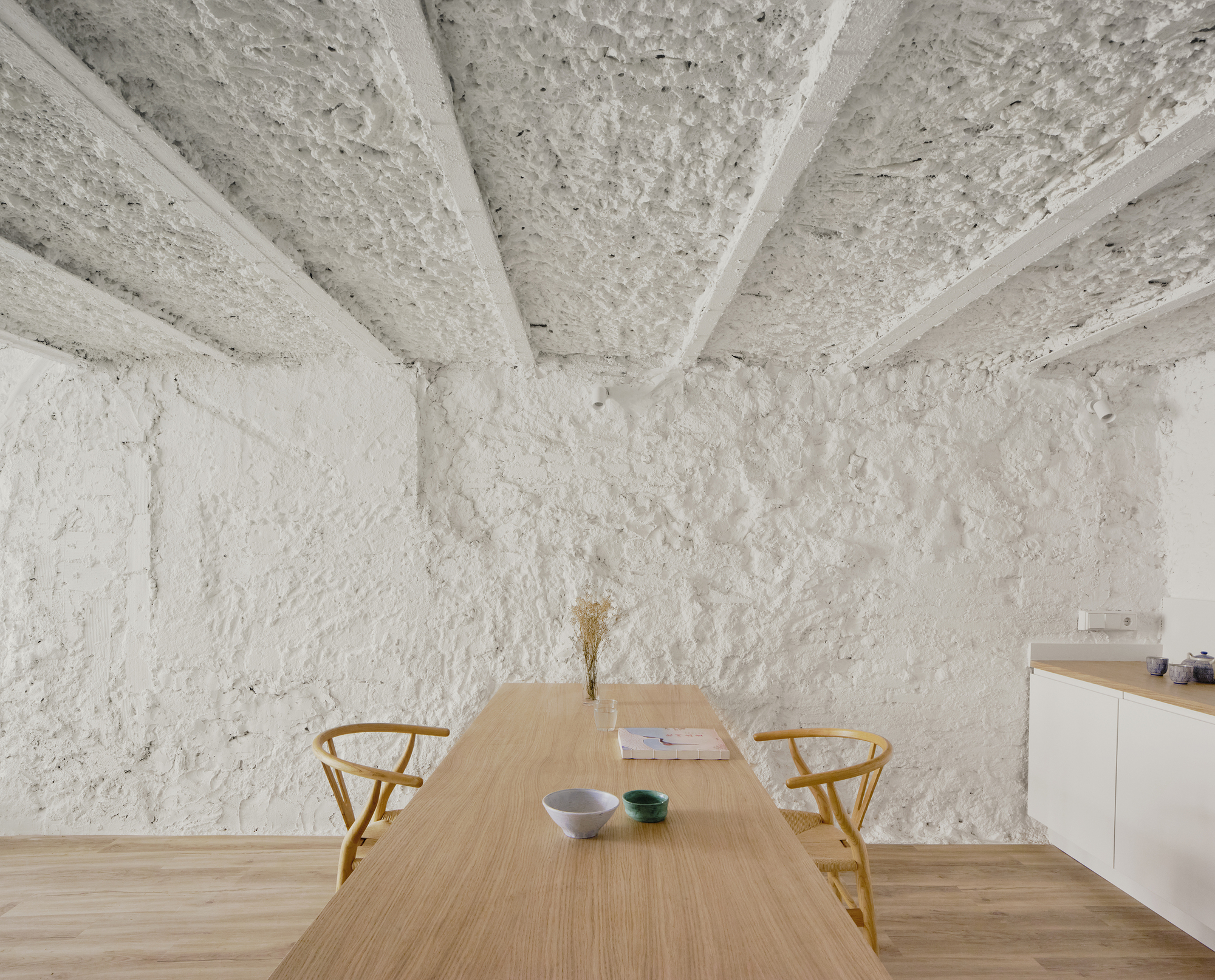 Corner of dining space with exposed structural ceiling and rough white plaster walls