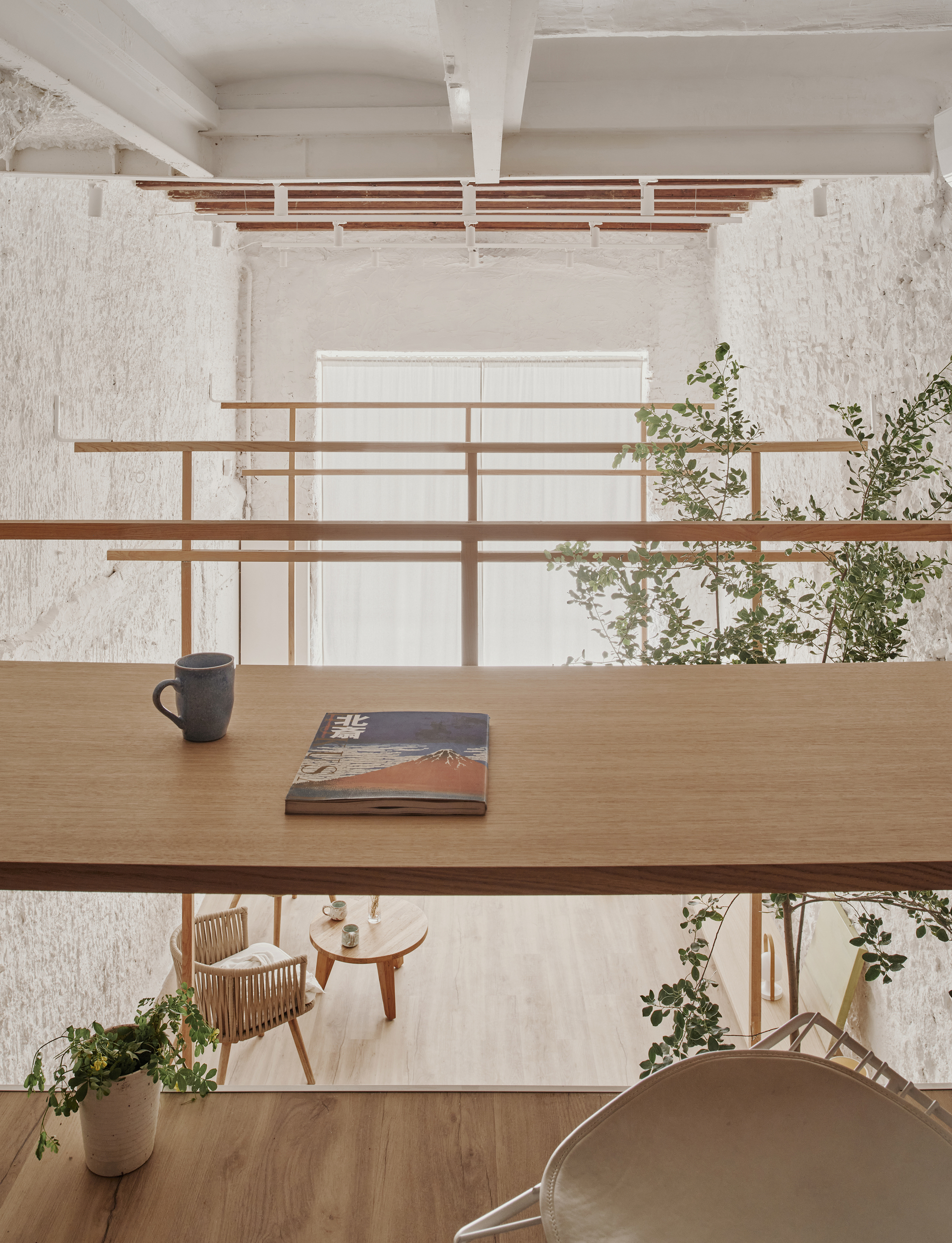 View from mezzanine workspace showing timber desk with mug and book overlooking the lower seating area