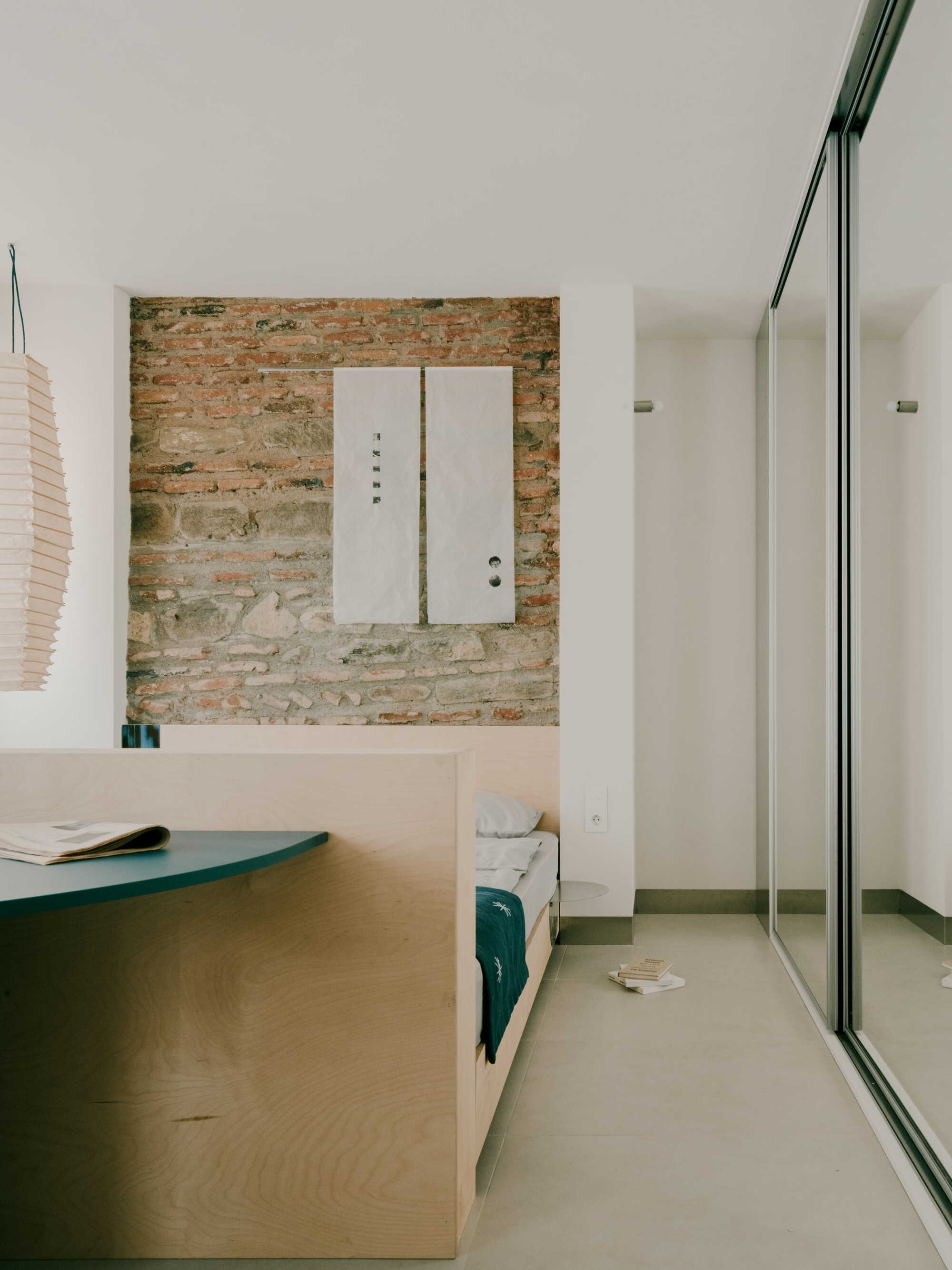 Interior bedroom with exposed brick wall, white security door, and full-height glazing on the right