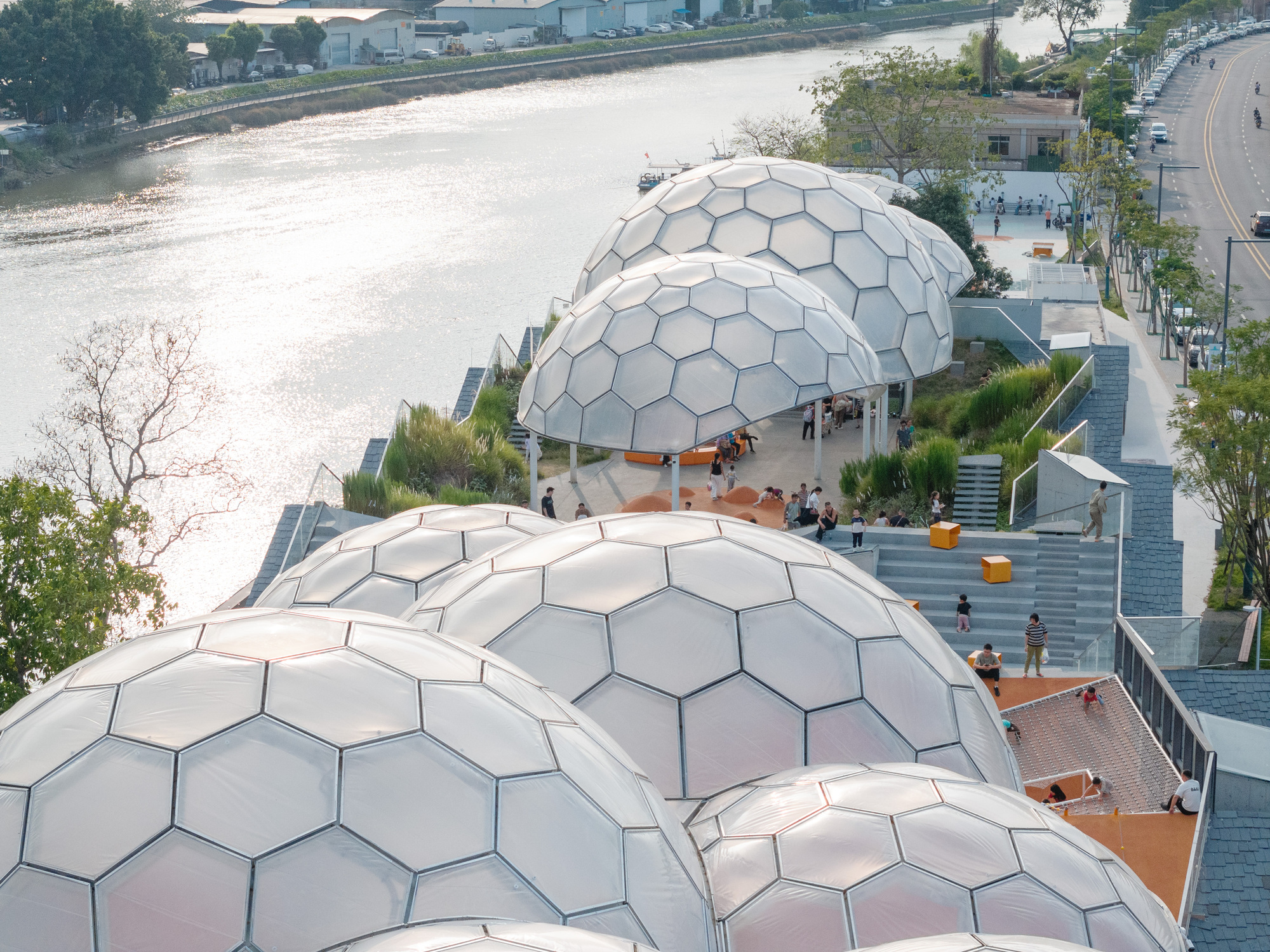 Aerial view of clustered hexagonal dome pavilions along a riverside promenade with visitors on tiered seating