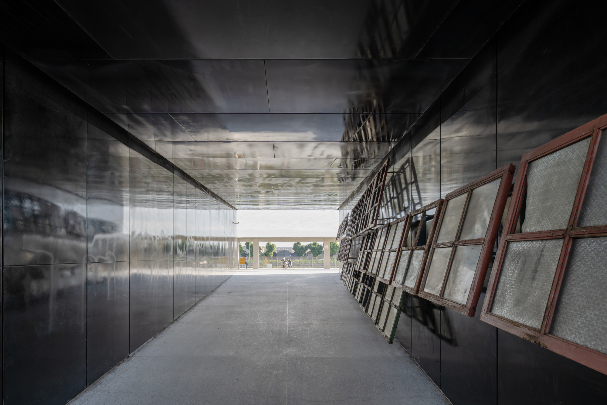 Corridor with reflective metal wall panels and angled wire mesh screens under a polished ceiling