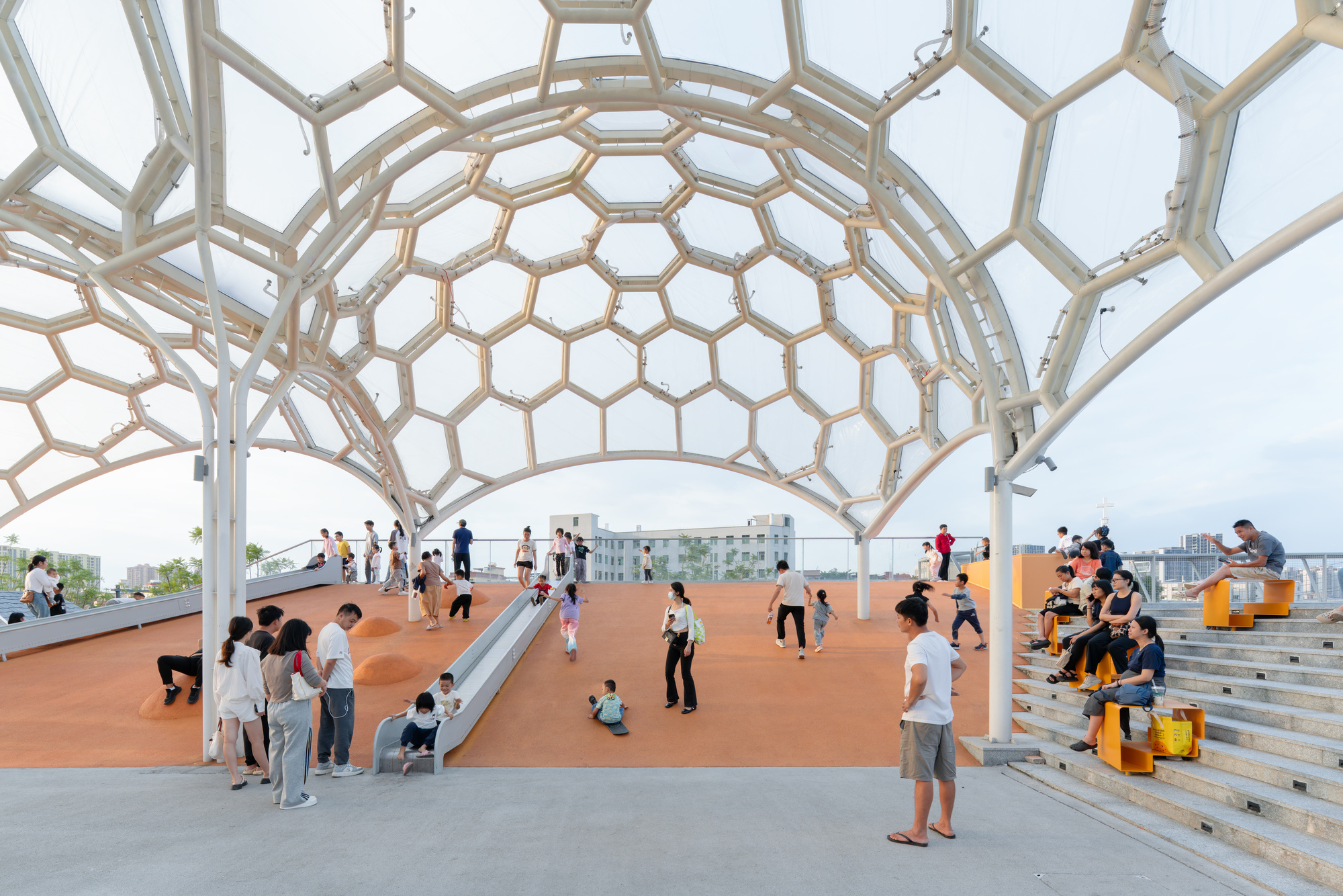 Wide view under the dome canopy showing visitors on orange flooring with timber stepped seating along the edge