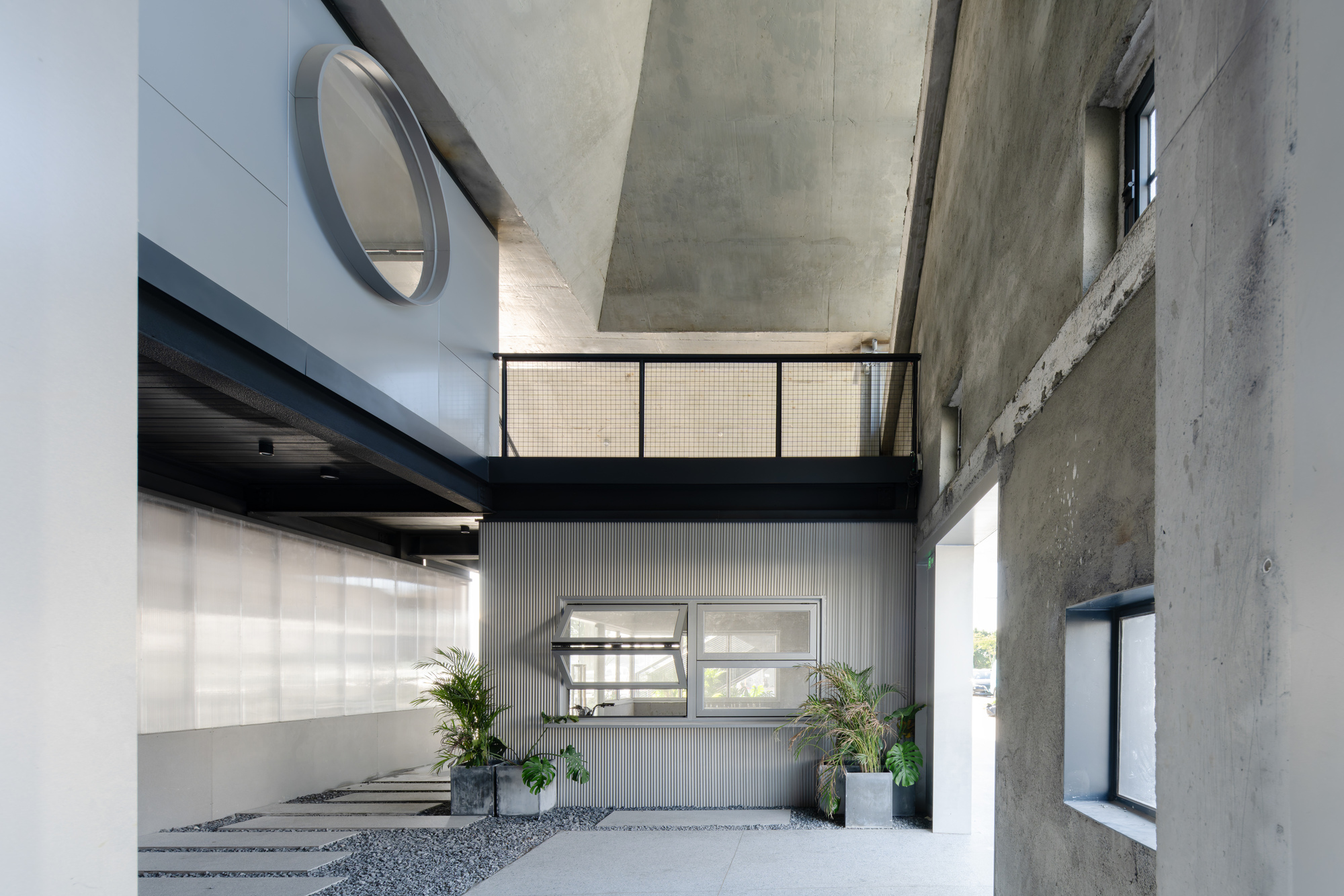 Covered entry courtyard with exposed concrete walls, corrugated metal cladding and potted plants flanking the entrance