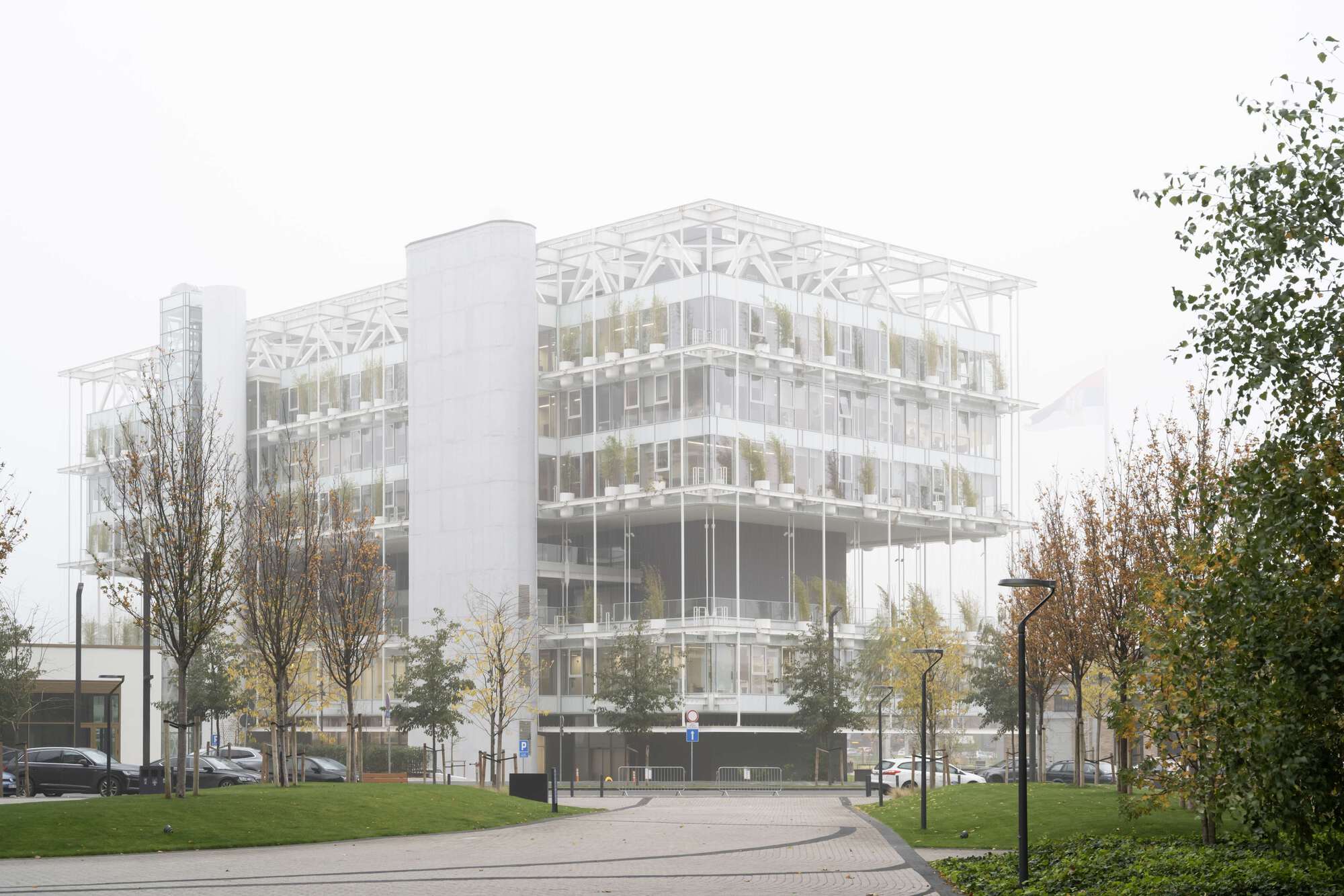 Glass and steel facade with exposed white truss structure viewed from the street on an overcast autumn day