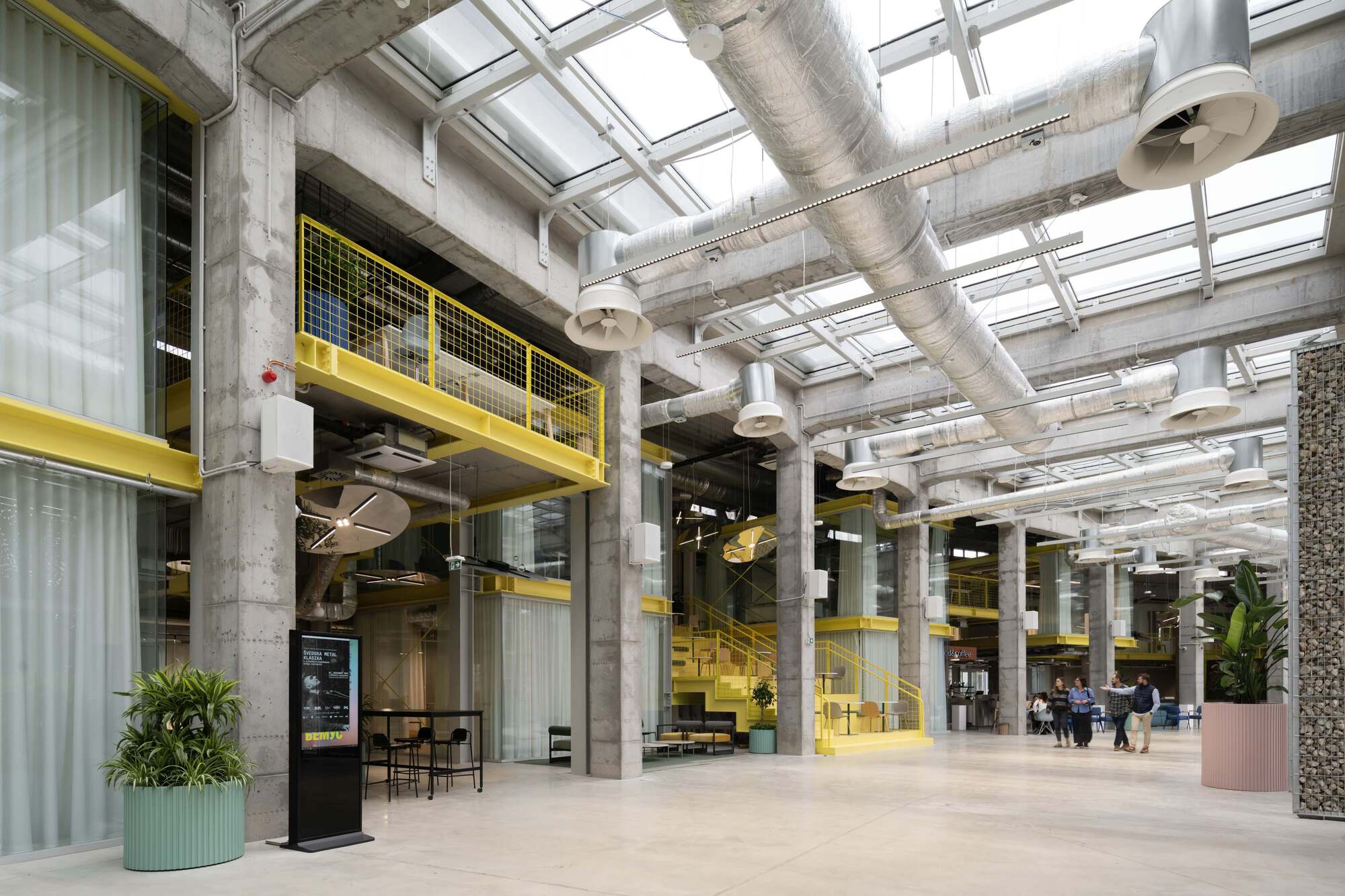 Interior atrium with exposed concrete columns, yellow mesh walkways and glazed skylight ceiling