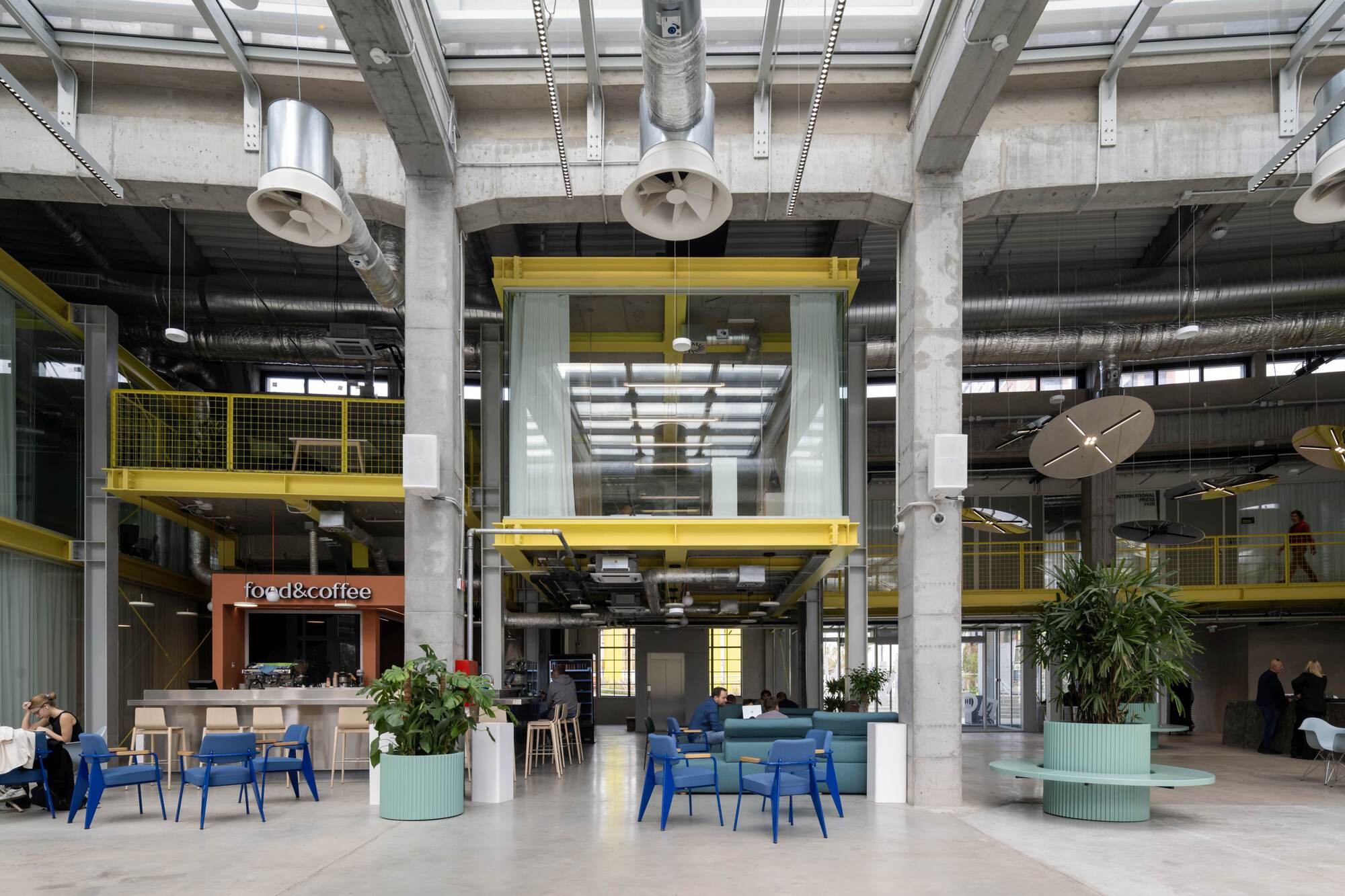 Ground floor lobby space with concrete structure, yellow metal railings and planted seating areas