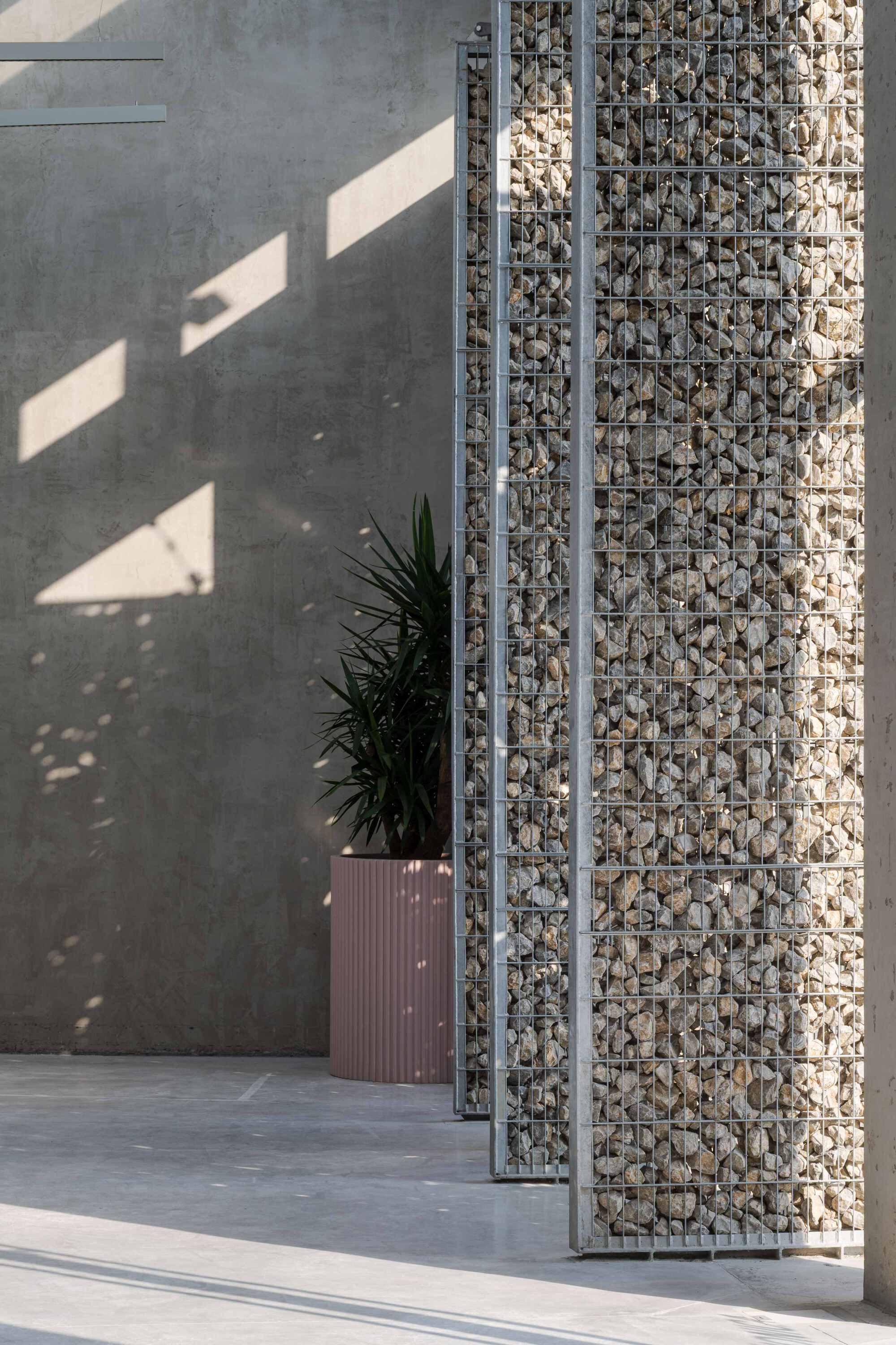 Gabion wall column filled with pale stones beside a potted plant in afternoon shadow