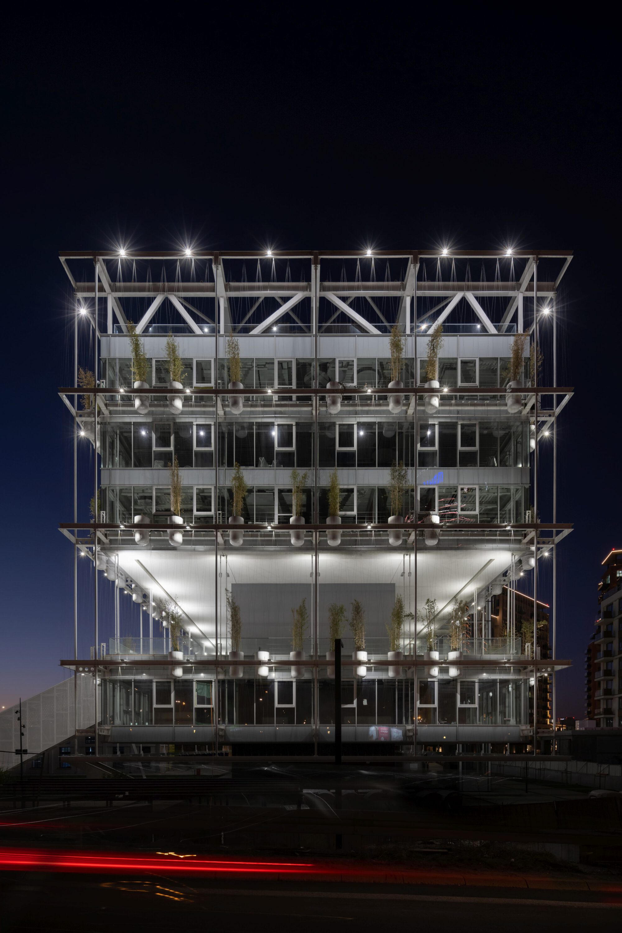 Five-story exposed steel frame building with planted terraces illuminated against a night sky