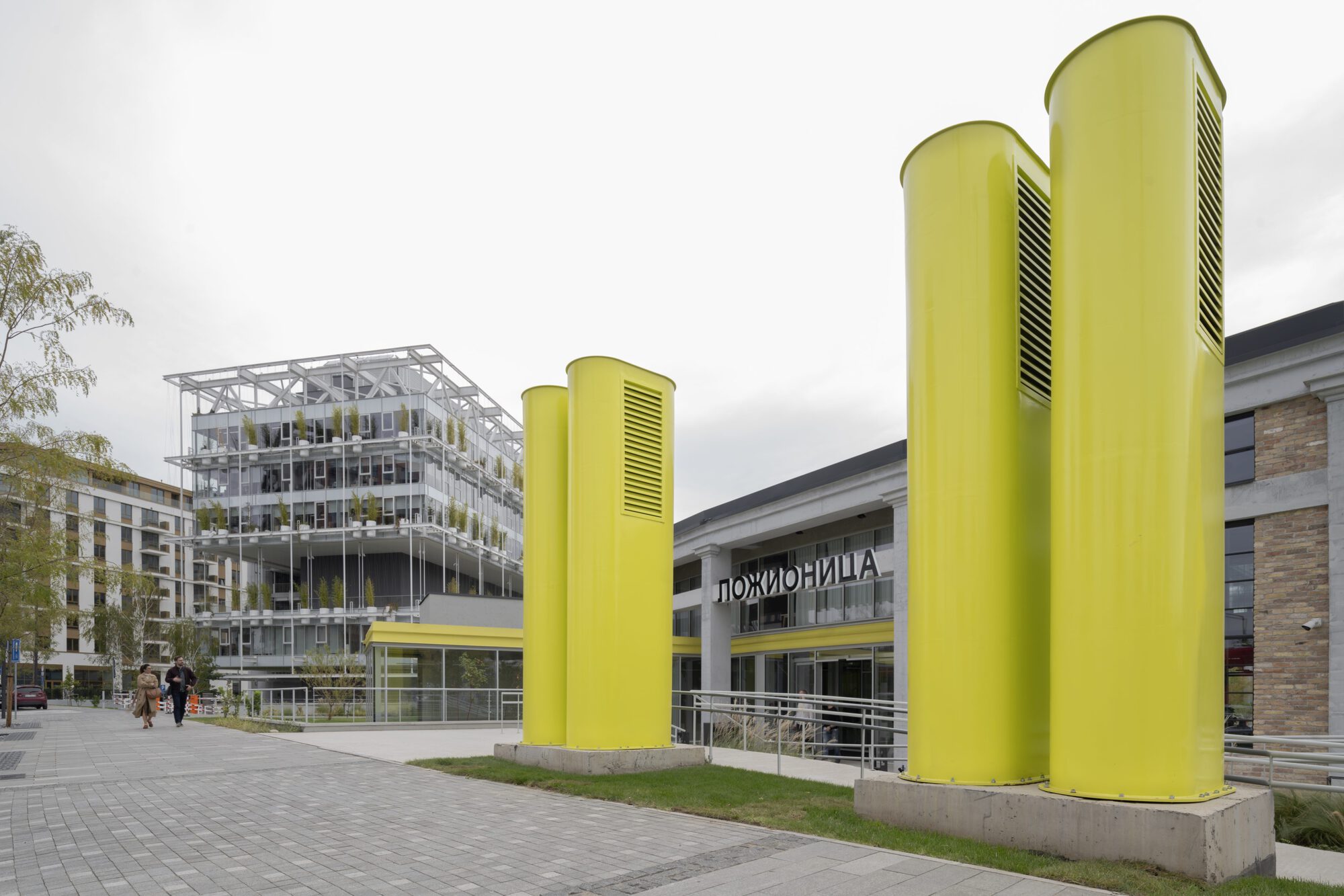 Three yellow ventilation towers with louvered openings standing in front of the plaza entrance