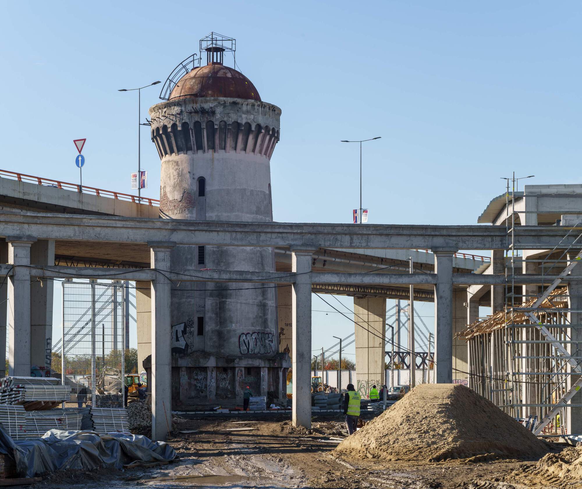 Weathered cylindrical tower with copper dome surrounded by construction site and concrete frame structure