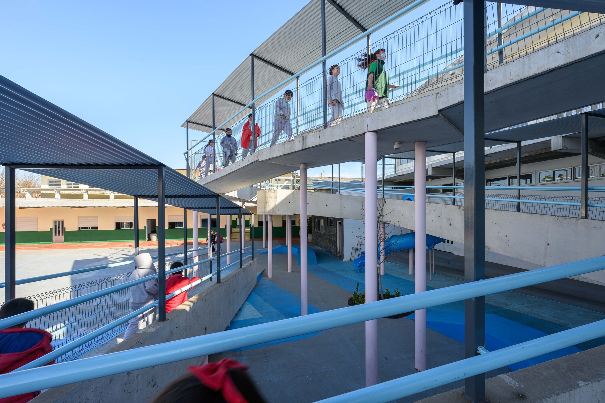 View of stacked concrete ramps and blue slide beneath a metal canopy with children ascending the upper level