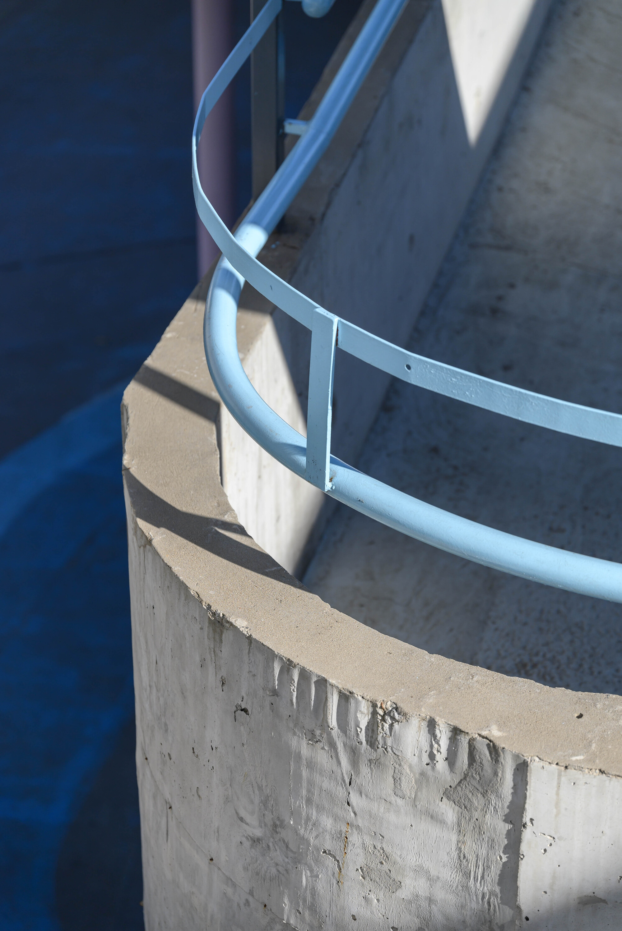 Detail of curved blue metal railing wrapping the edge of a cast concrete planter in sunlight