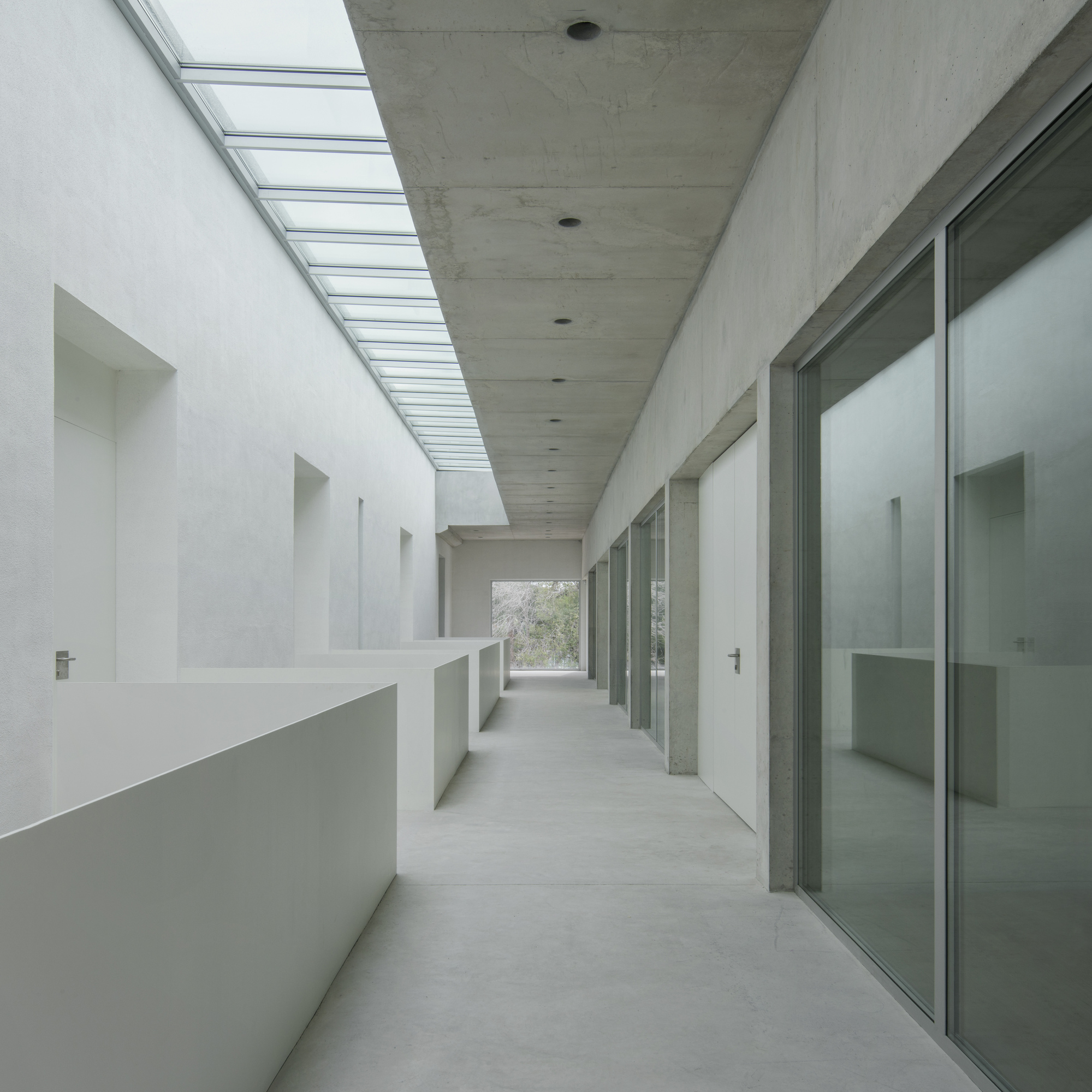 Interior corridor with continuous skylight running along concrete ceiling between white wall and glazed doors