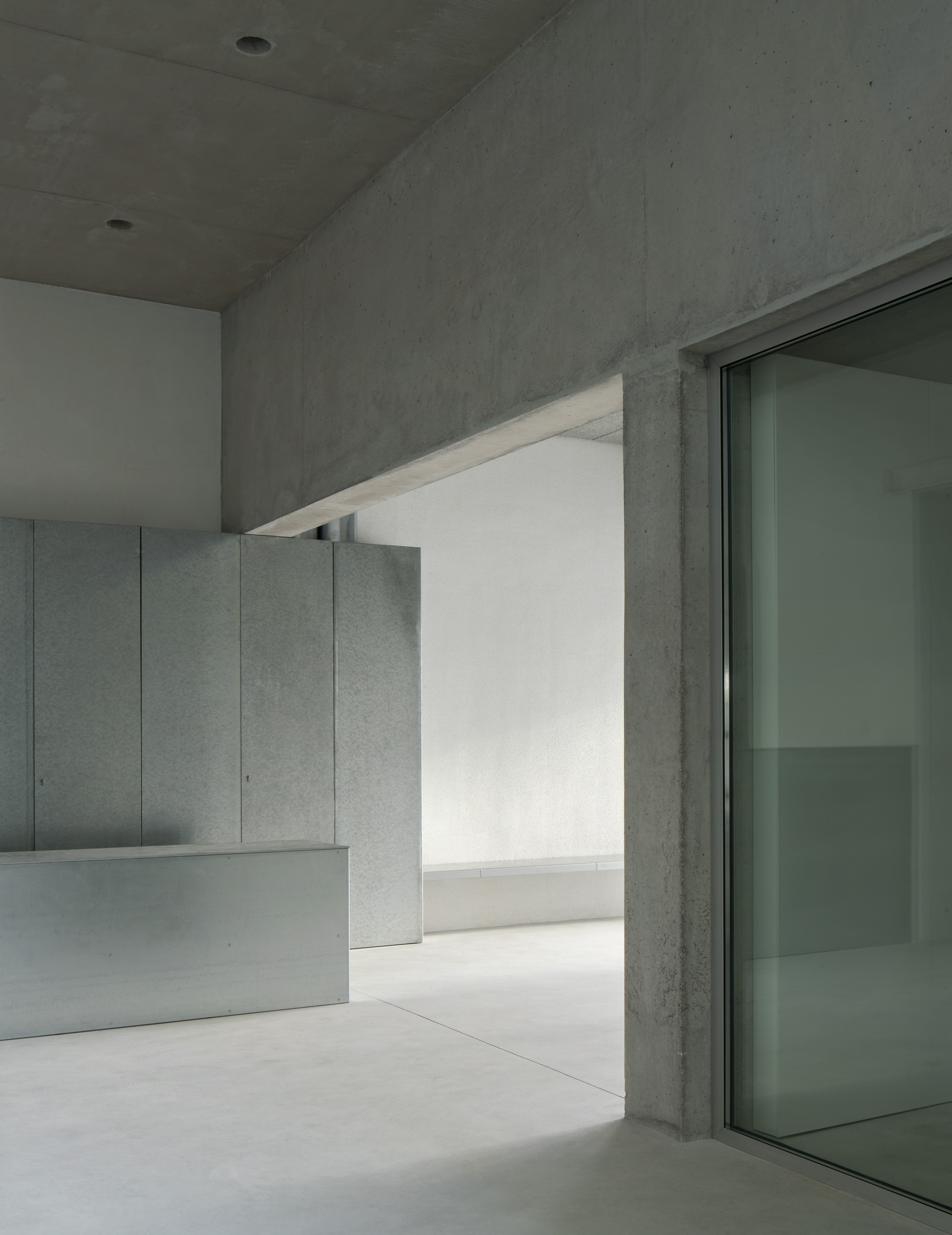 Corner detail where concrete wall meets ceiling plane beside a glazed door opening