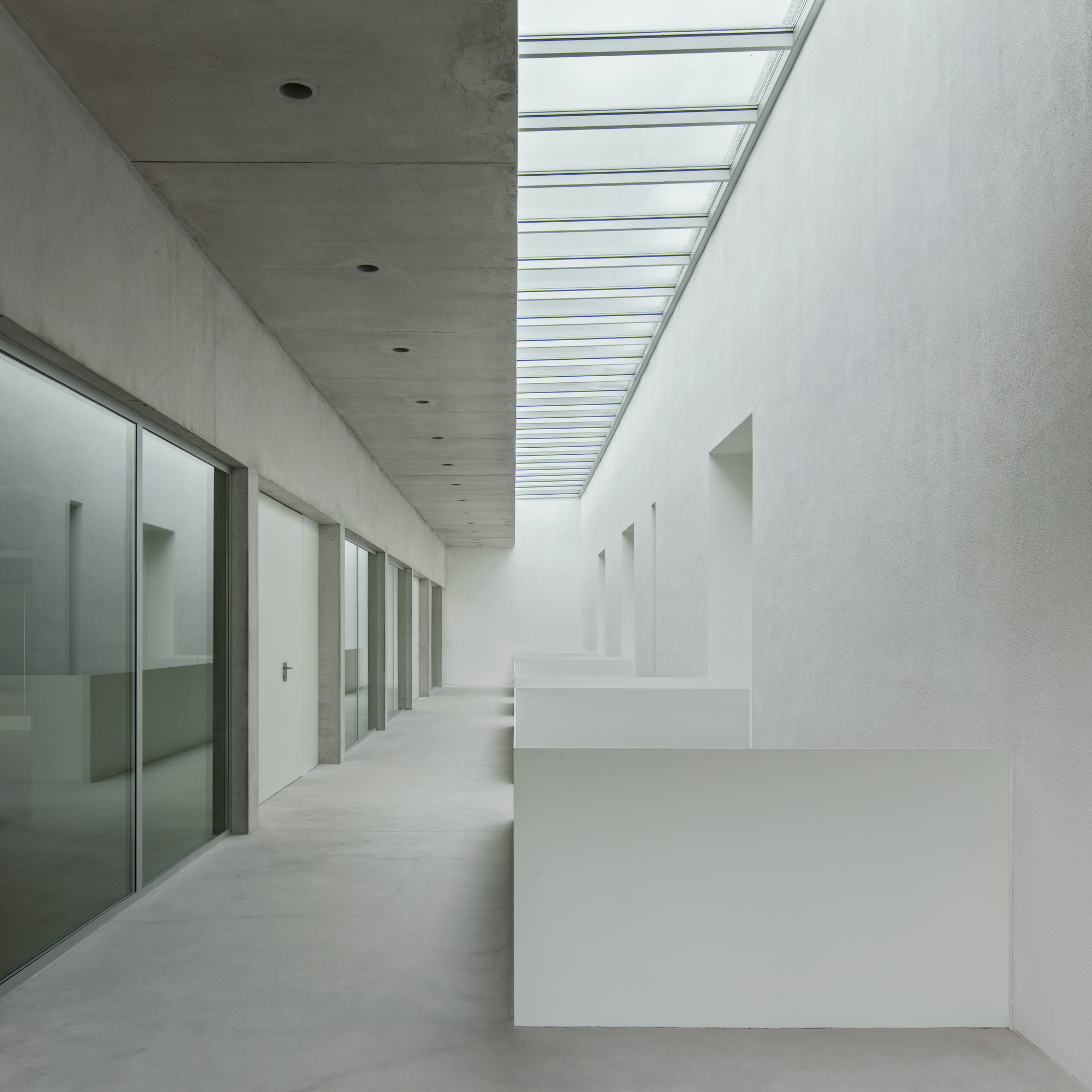 Corridor with glass partitions and concrete ceiling illuminated by a continuous skylight
