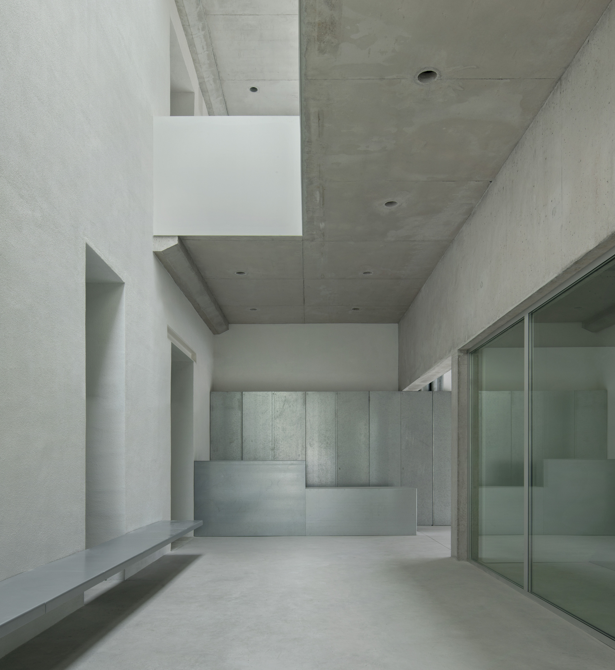 Gallery space with concrete walls and a reception desk under exposed concrete ceiling beams