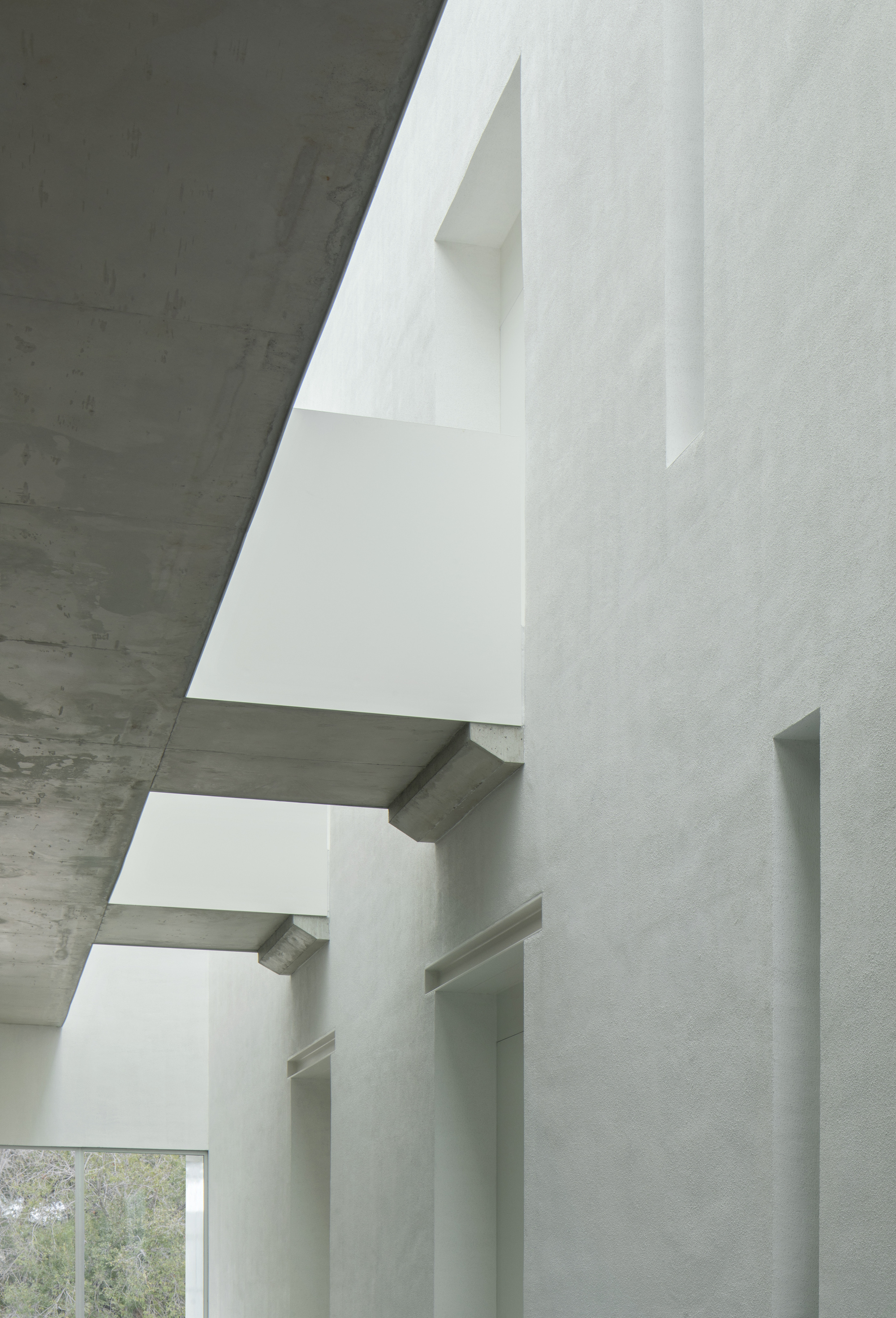 Vertical view of stacked white plaster volumes cantilevering between board-formed concrete ceilings