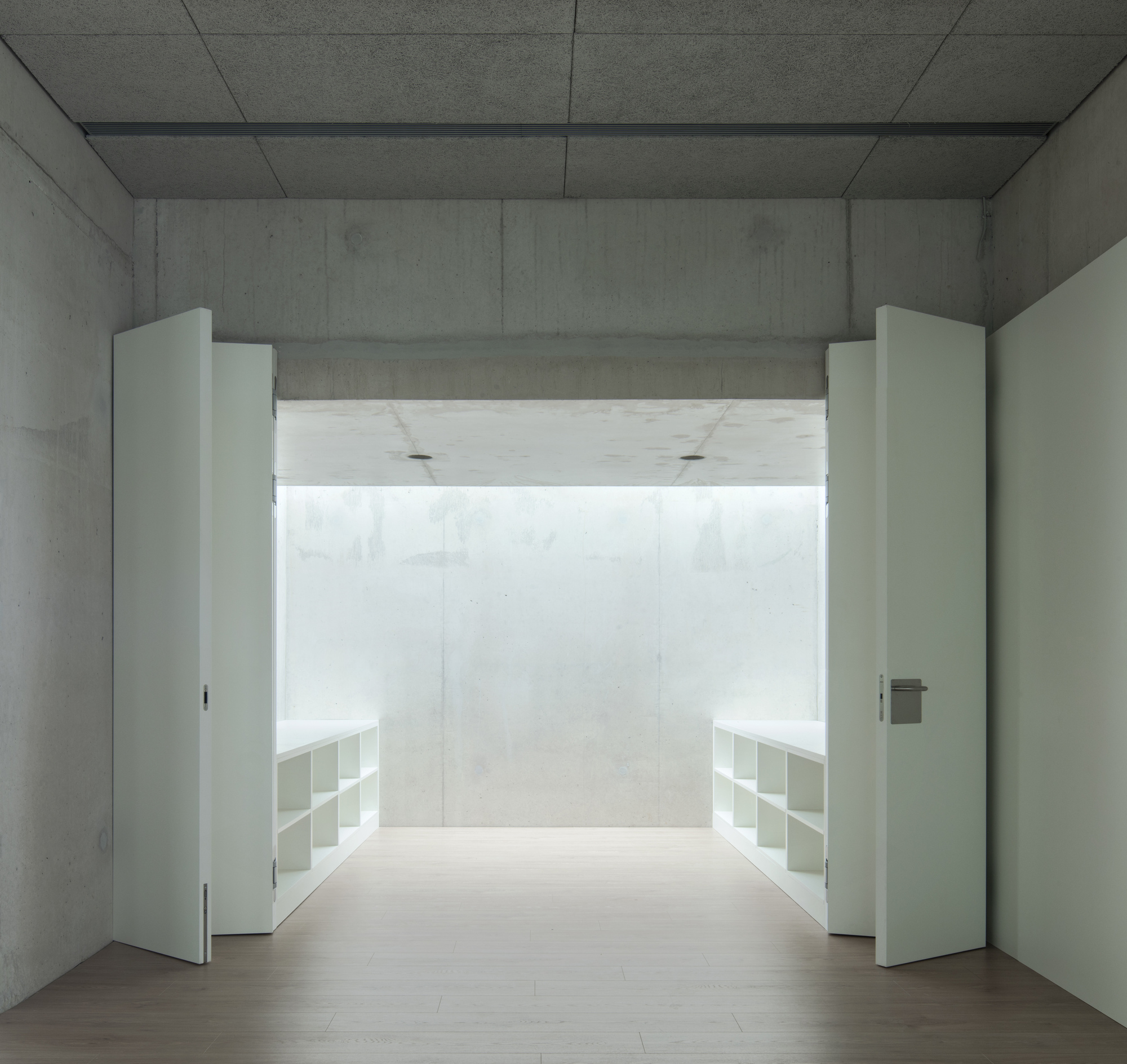 Concrete room with white double doors opening to a bright space with built-in shelving