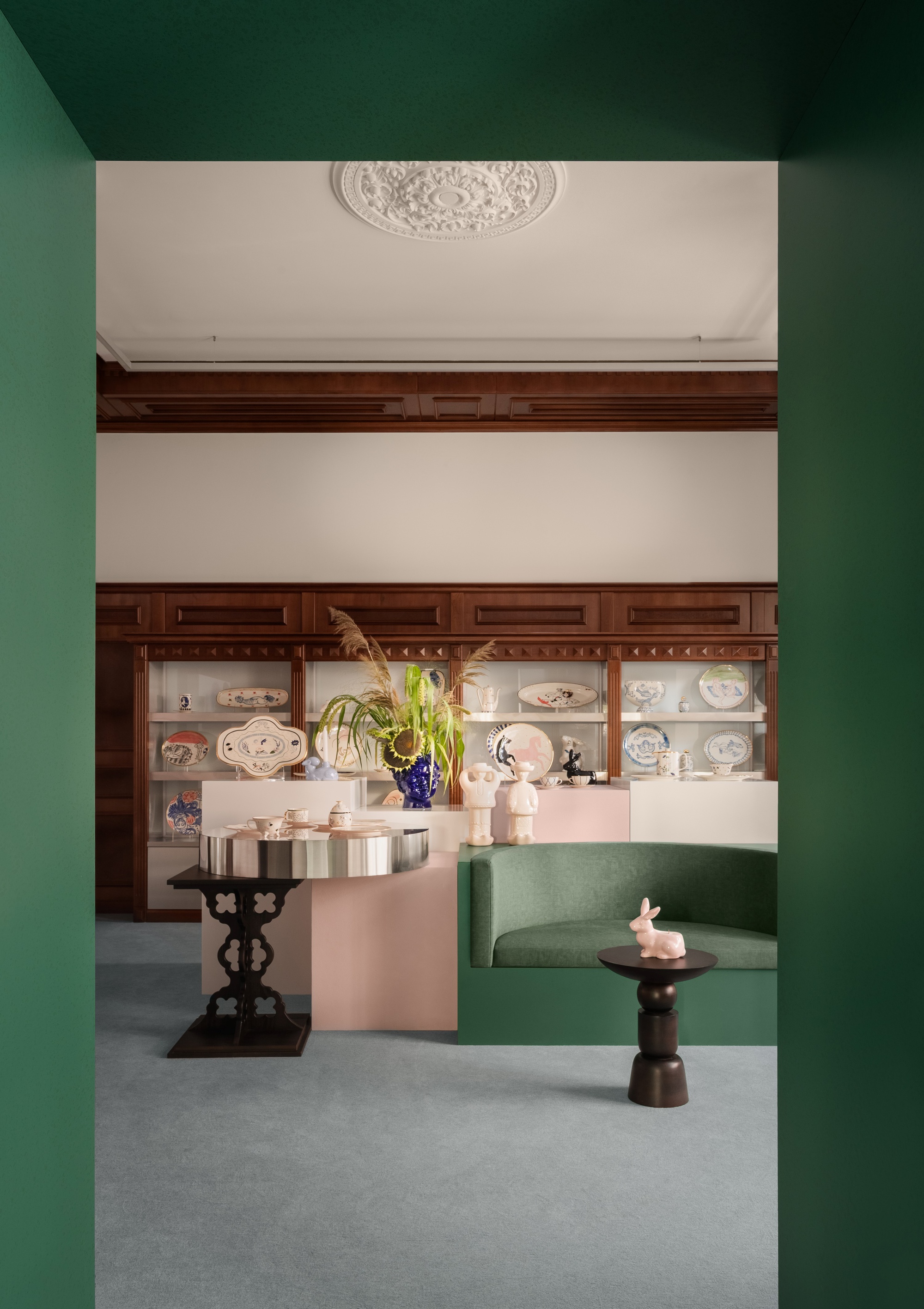 View through a green doorway into a reception room with paneled display cabinets and ornamental ceiling medallion