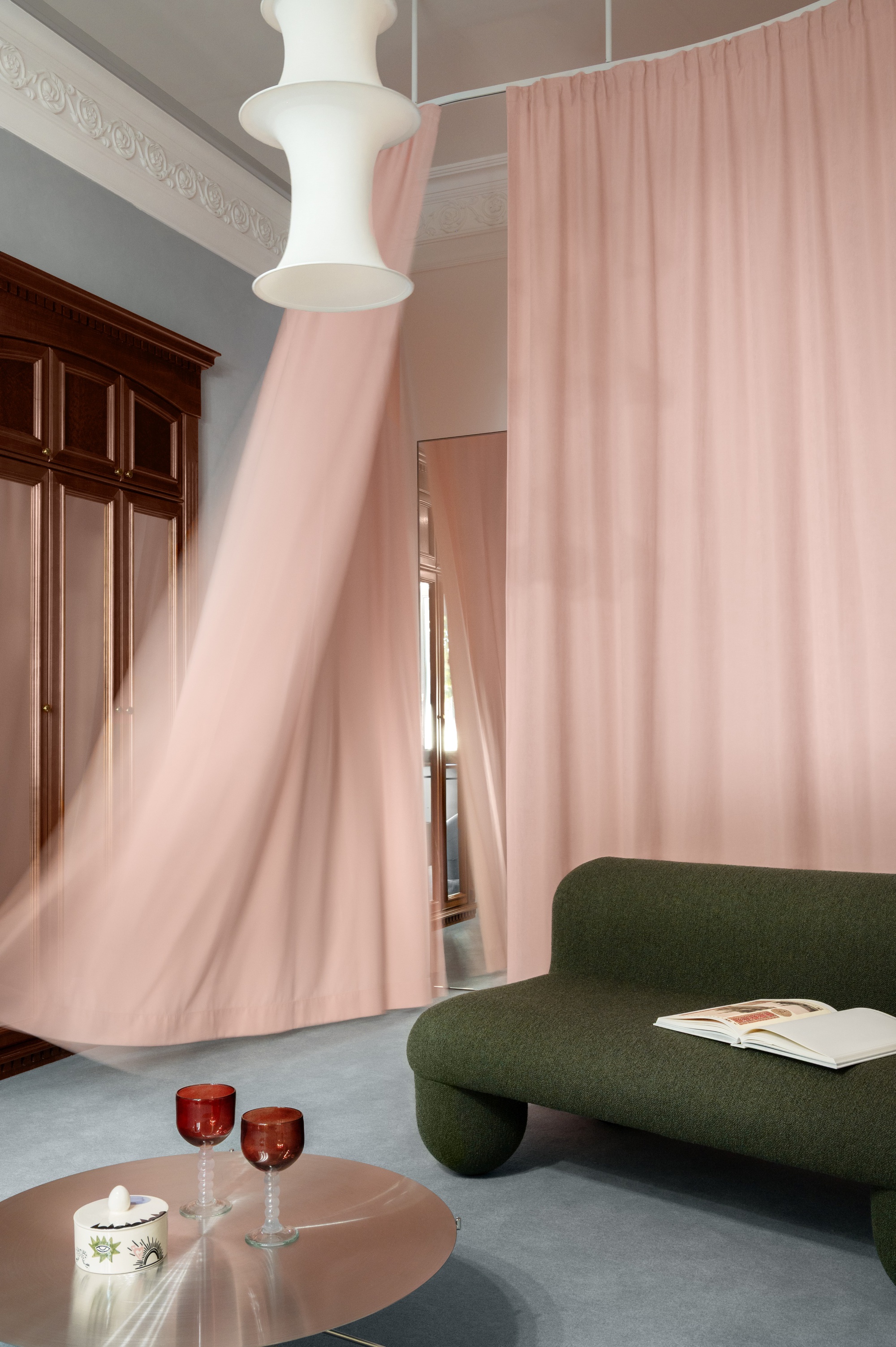 White sculptural column wrapped with flowing pink fabric beside a green upholstered sofa