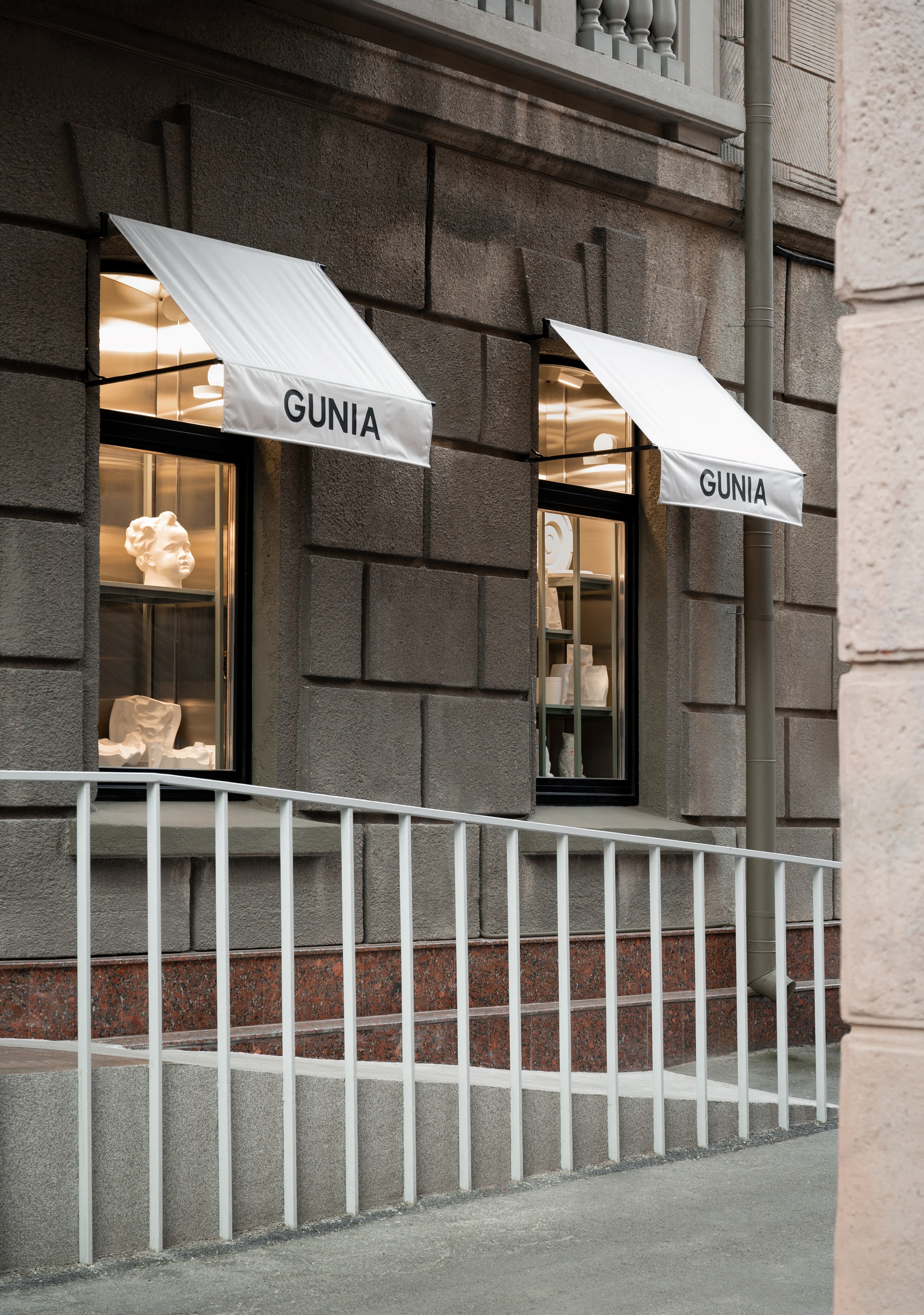 Street facade with rusticated stone base, two storefront windows with white canvas awnings, and white metal railing