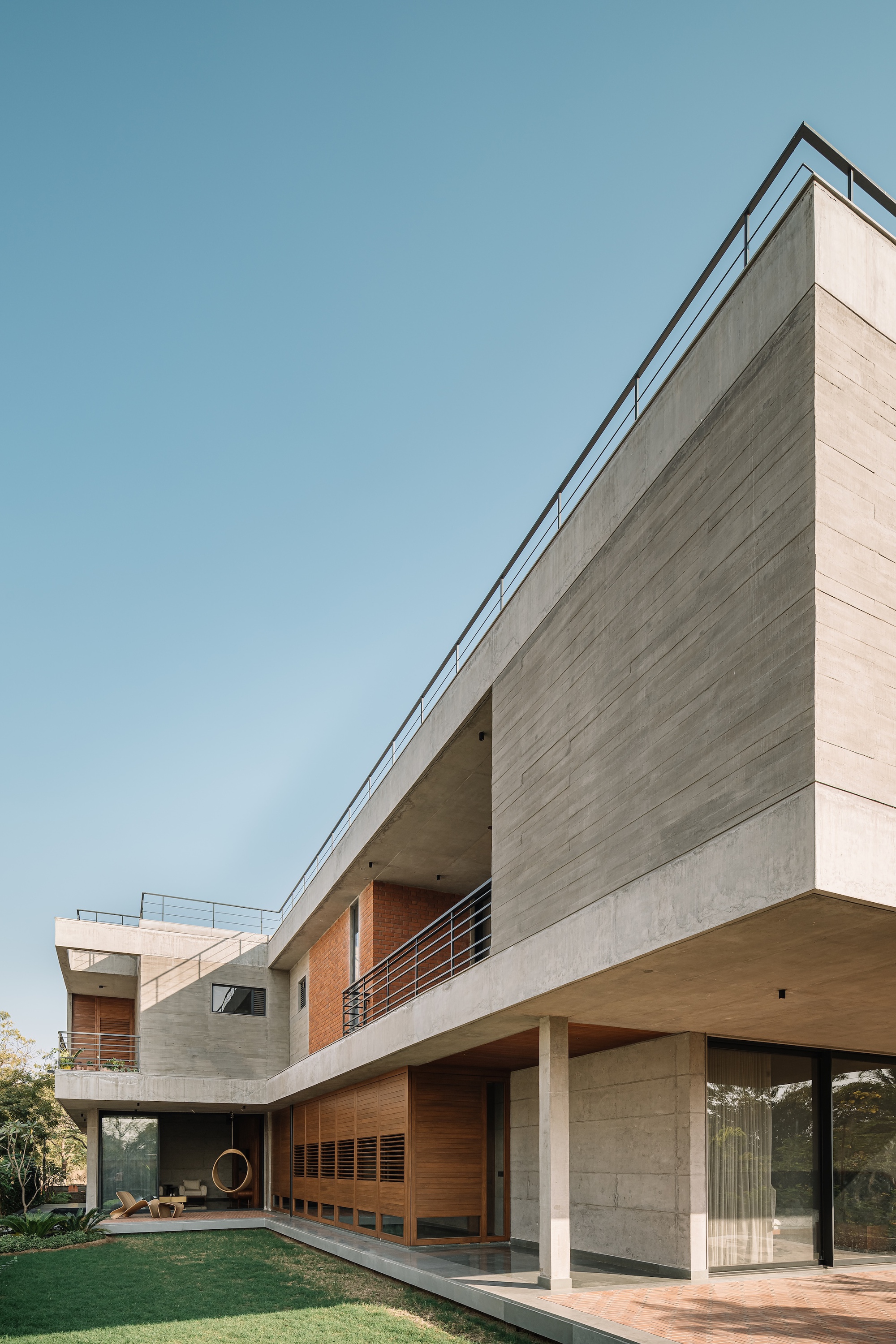 Angular concrete and timber facade with horizontal louvres and open terrace overlooking a garden lawn