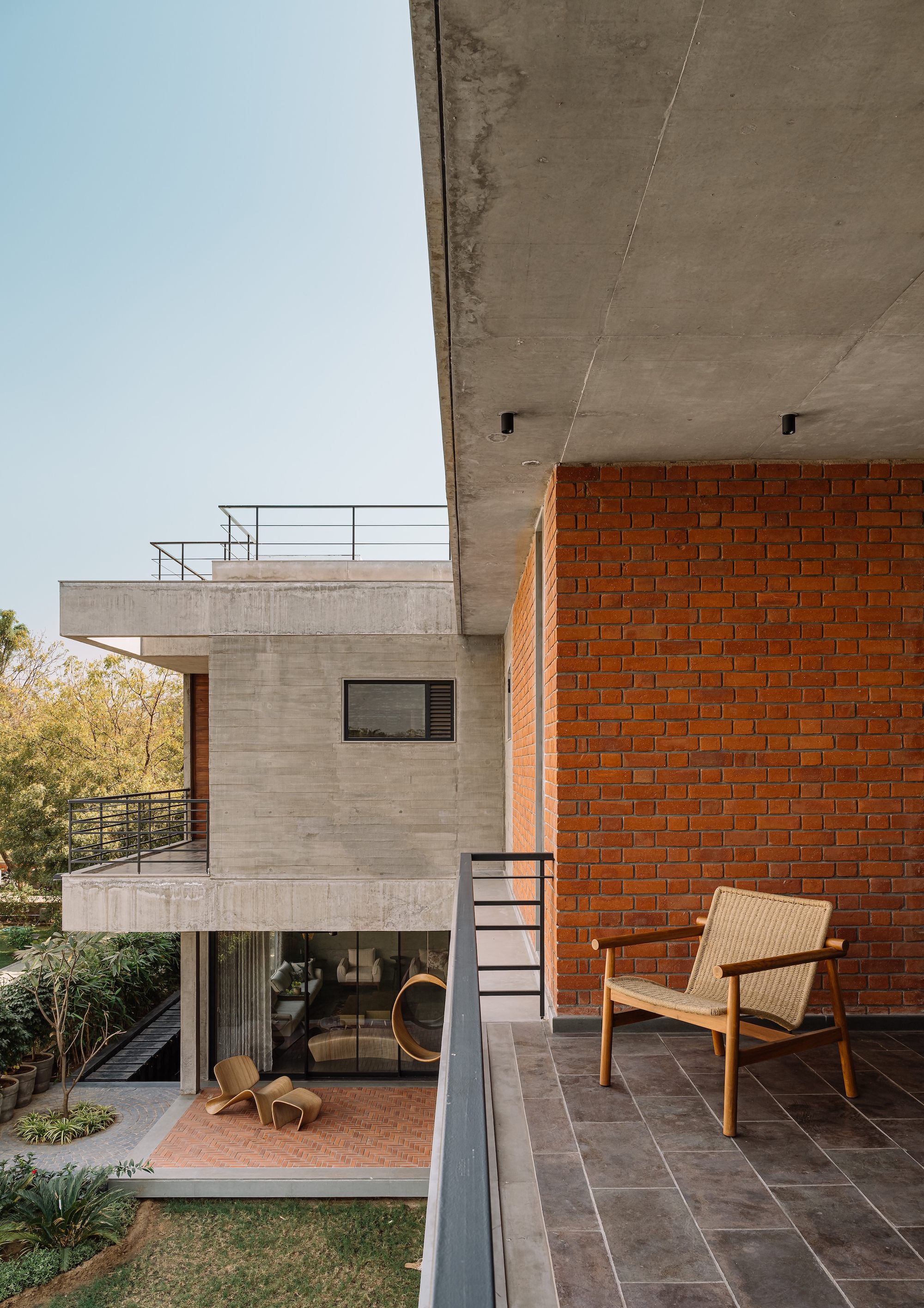 Covered terrace with red brick wall, wicker lounge chair, and view to concrete volumes beyond