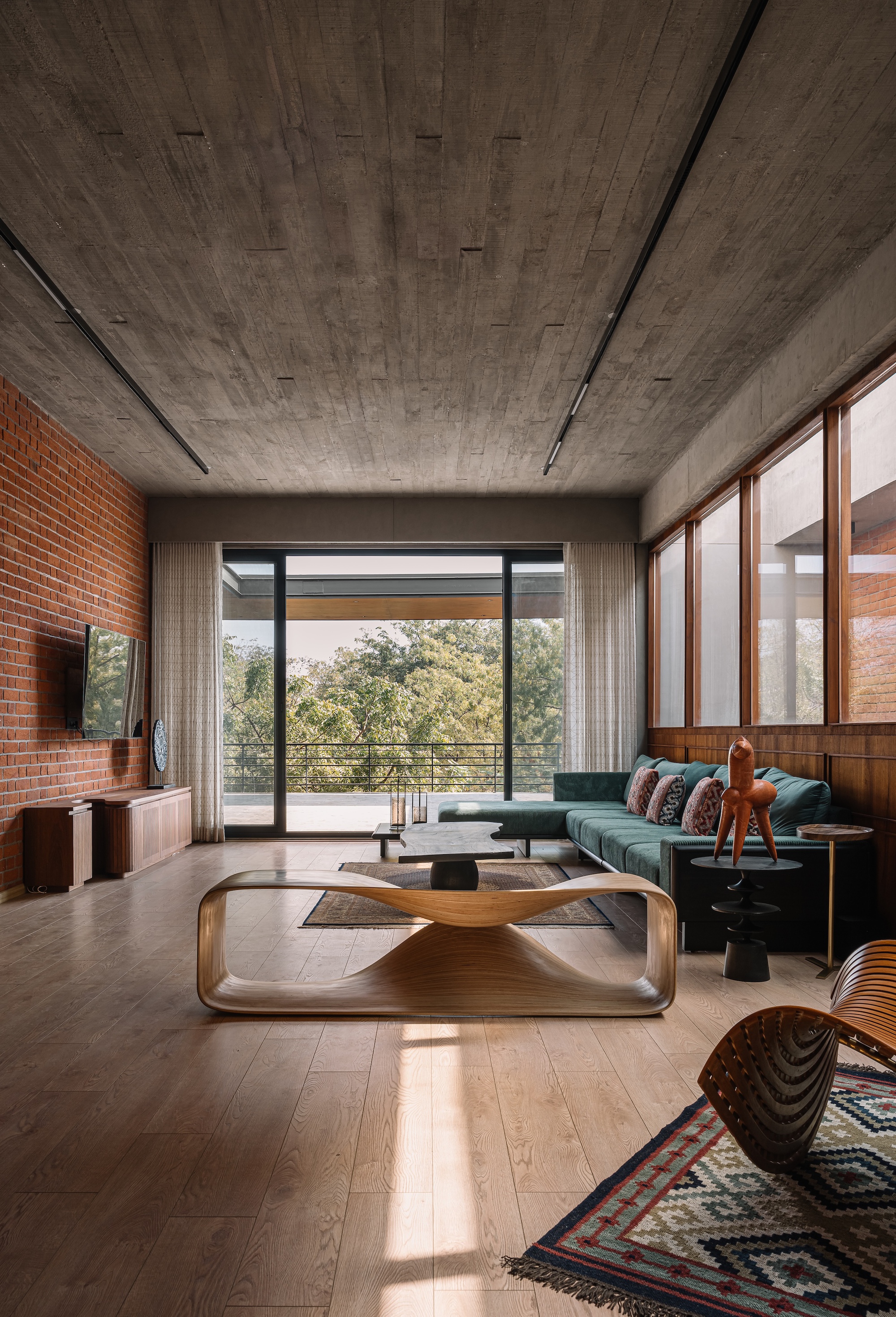Living room with board-formed concrete ceiling, exposed brick wall, and glazed doors opening to treetops