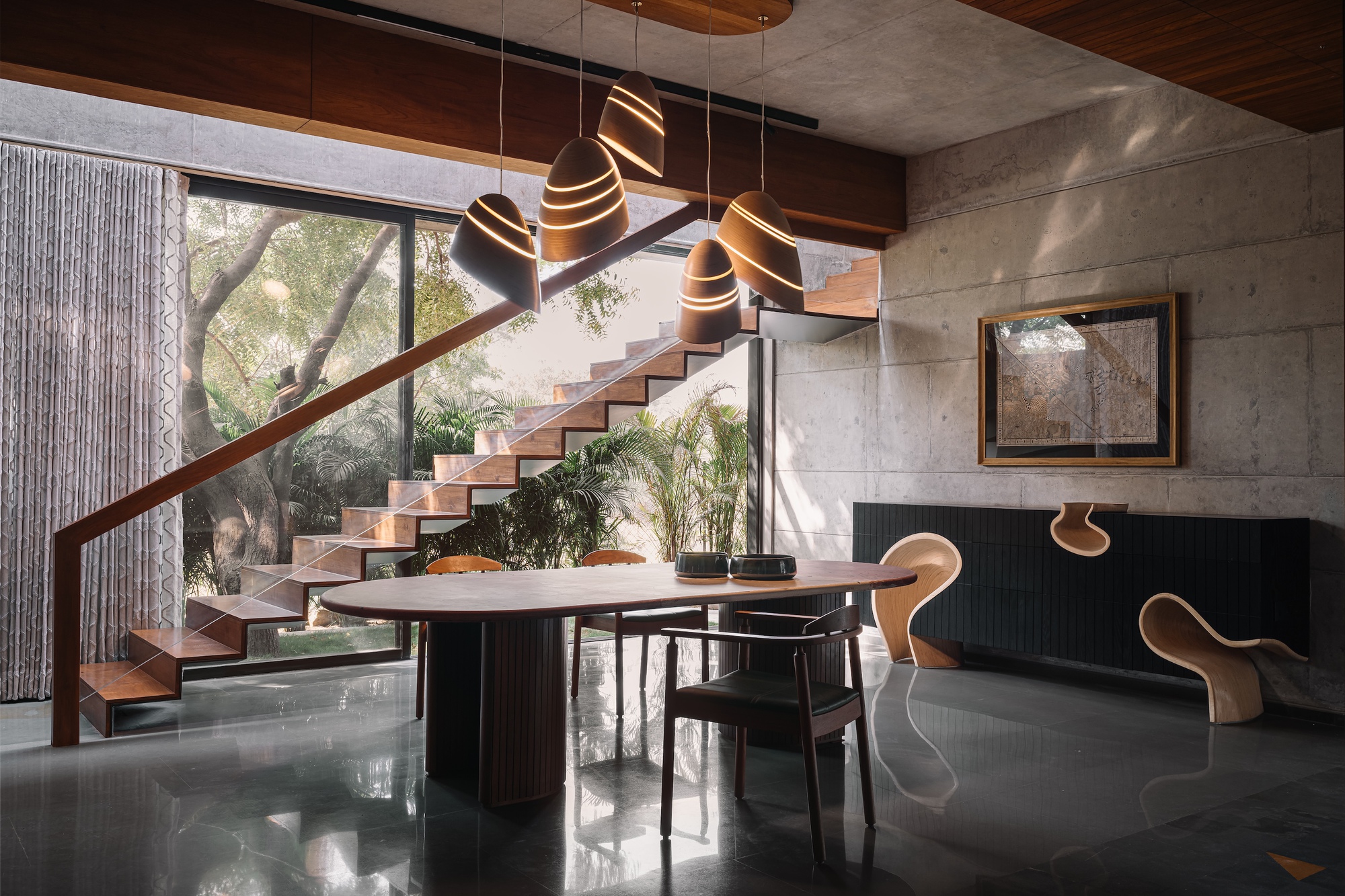 Open space showing sculptural staircase, concrete walls, polished stone floor with triangular inlays, and clustered pendant lights