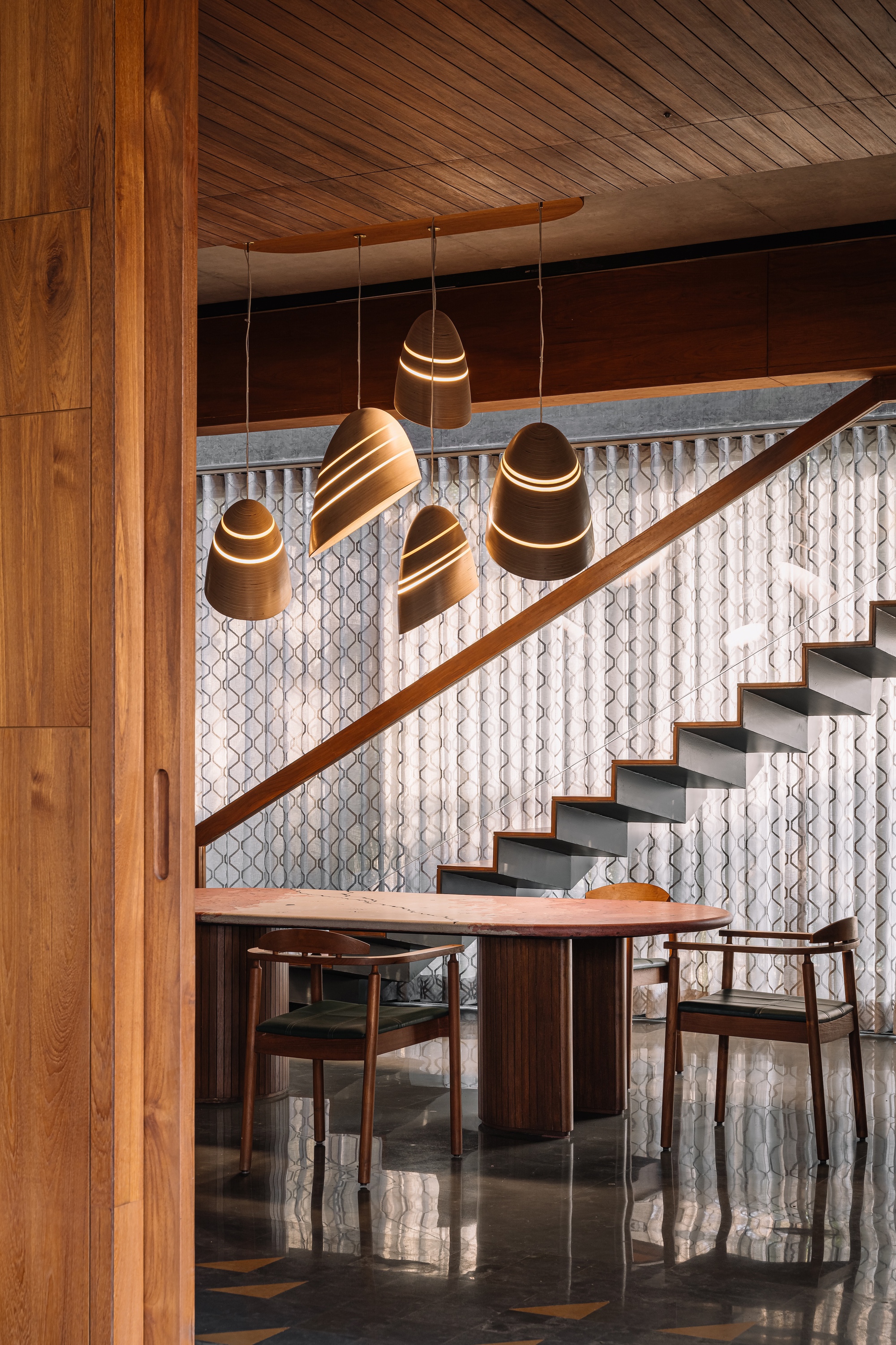 Close-up of sculptural timber pendant lights hanging beside cantilevered staircase with white relief-pattern screen wall