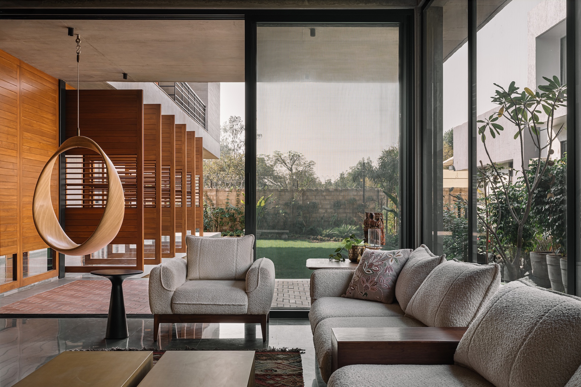 Living room with floor-to-ceiling glazing opening onto a lawn and timber-slatted staircase beyond