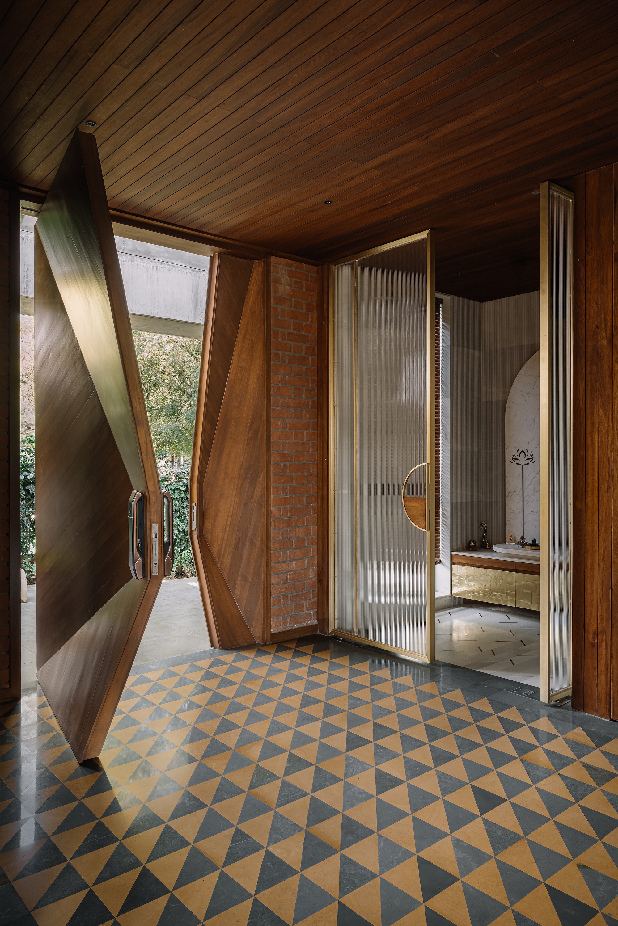Entry vestibule with angled timber pivot door and geometric floor tile in gold and grey triangles