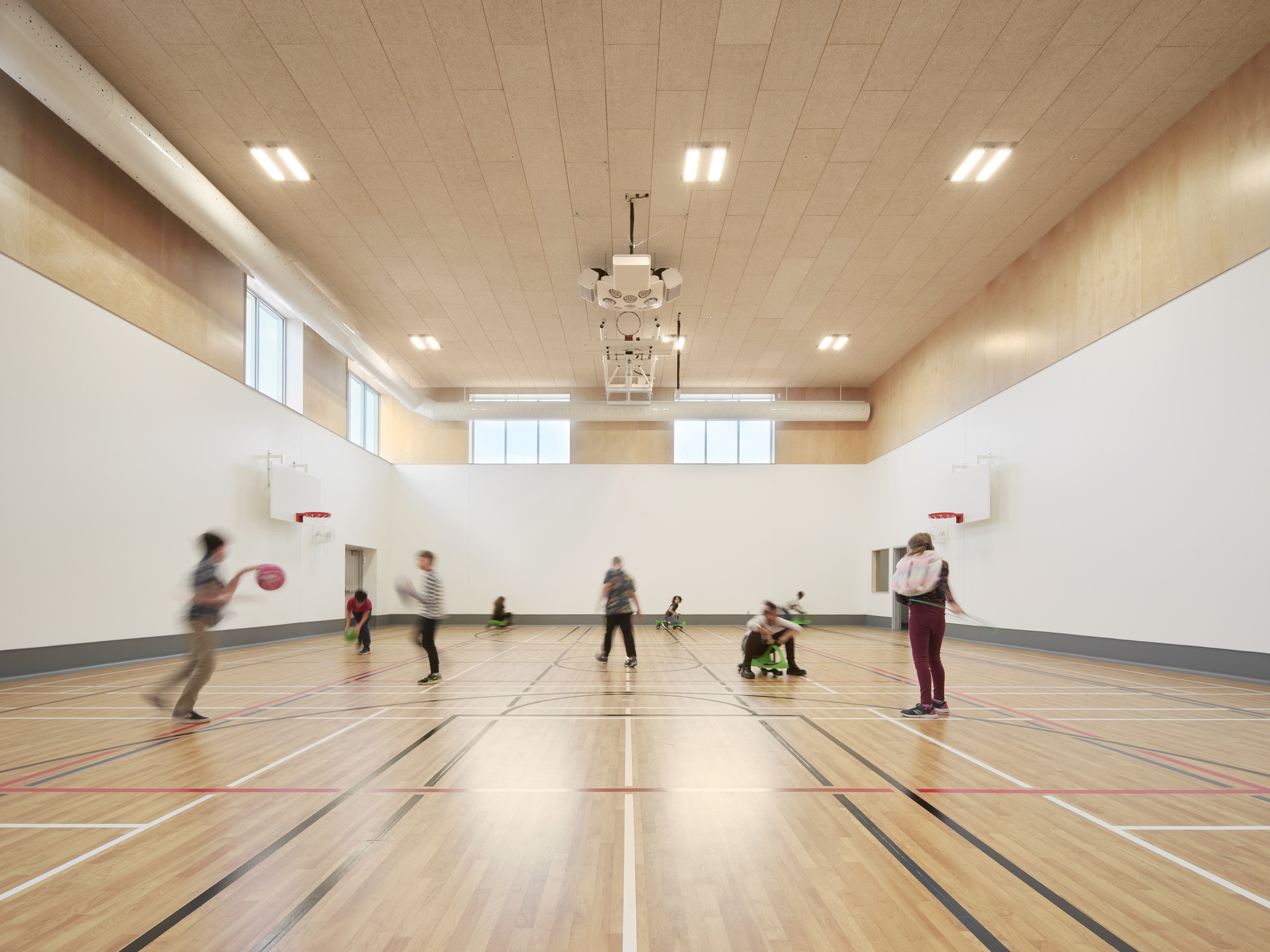 Gymnasium with timber floor and plywood ceiling where children play basketball in motion blur