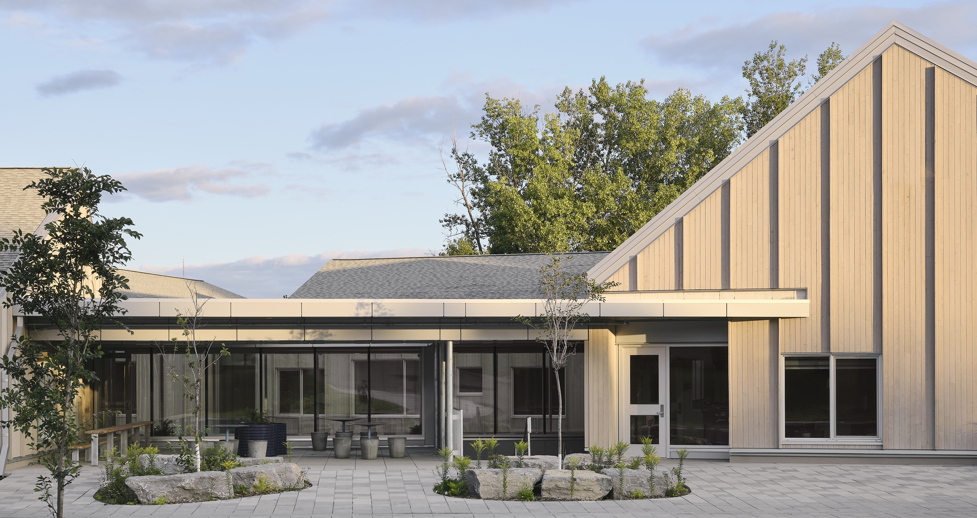 Courtyard view of the vertical timber-clad gable end and single-storey glazed wing at dusk