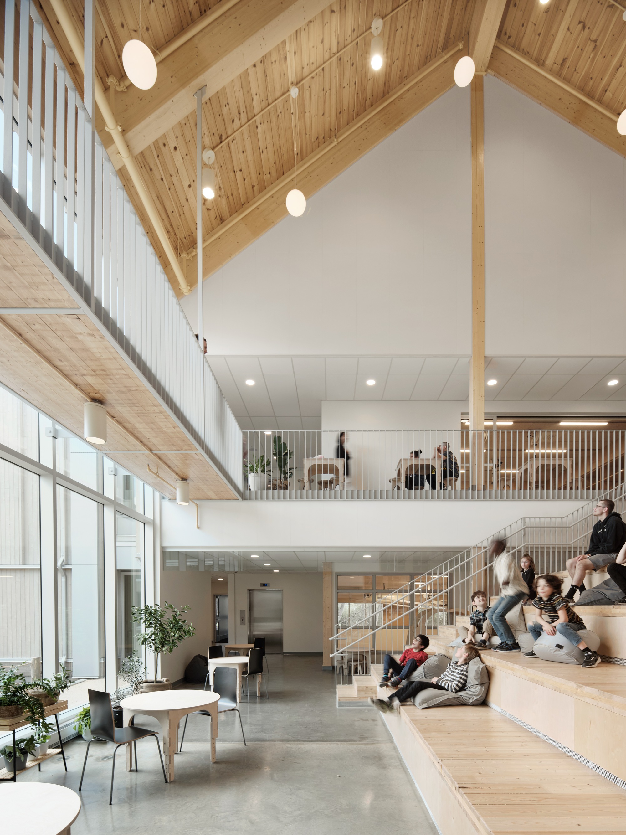 Double-height atrium with timber-clad vaulted ceiling and wide timber bleacher steps occupied by students