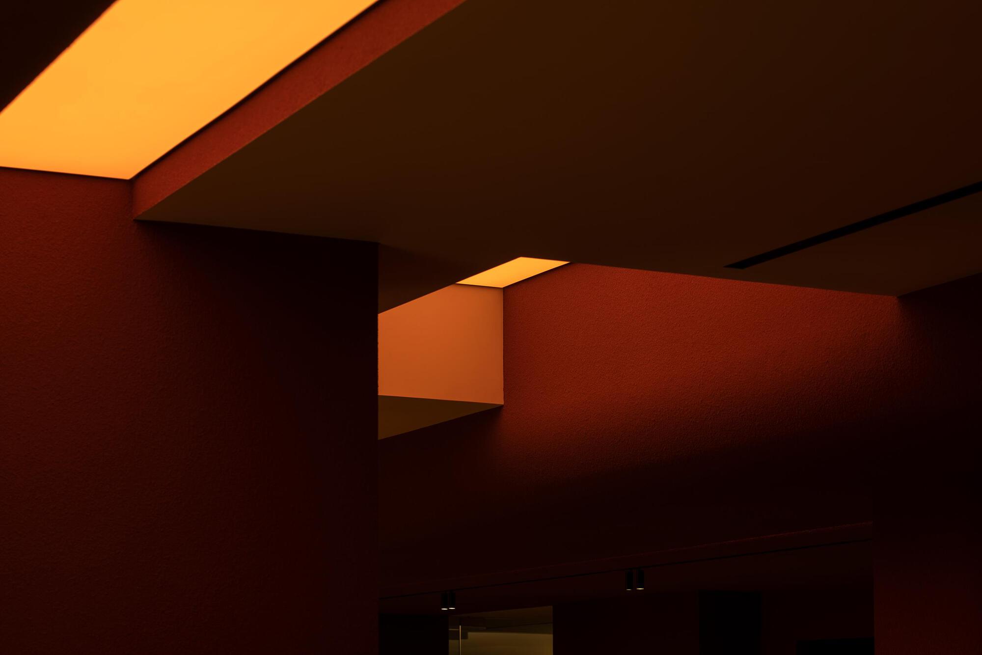 Overlapping recessed ceiling planes with concealed lighting creating layered amber shadows