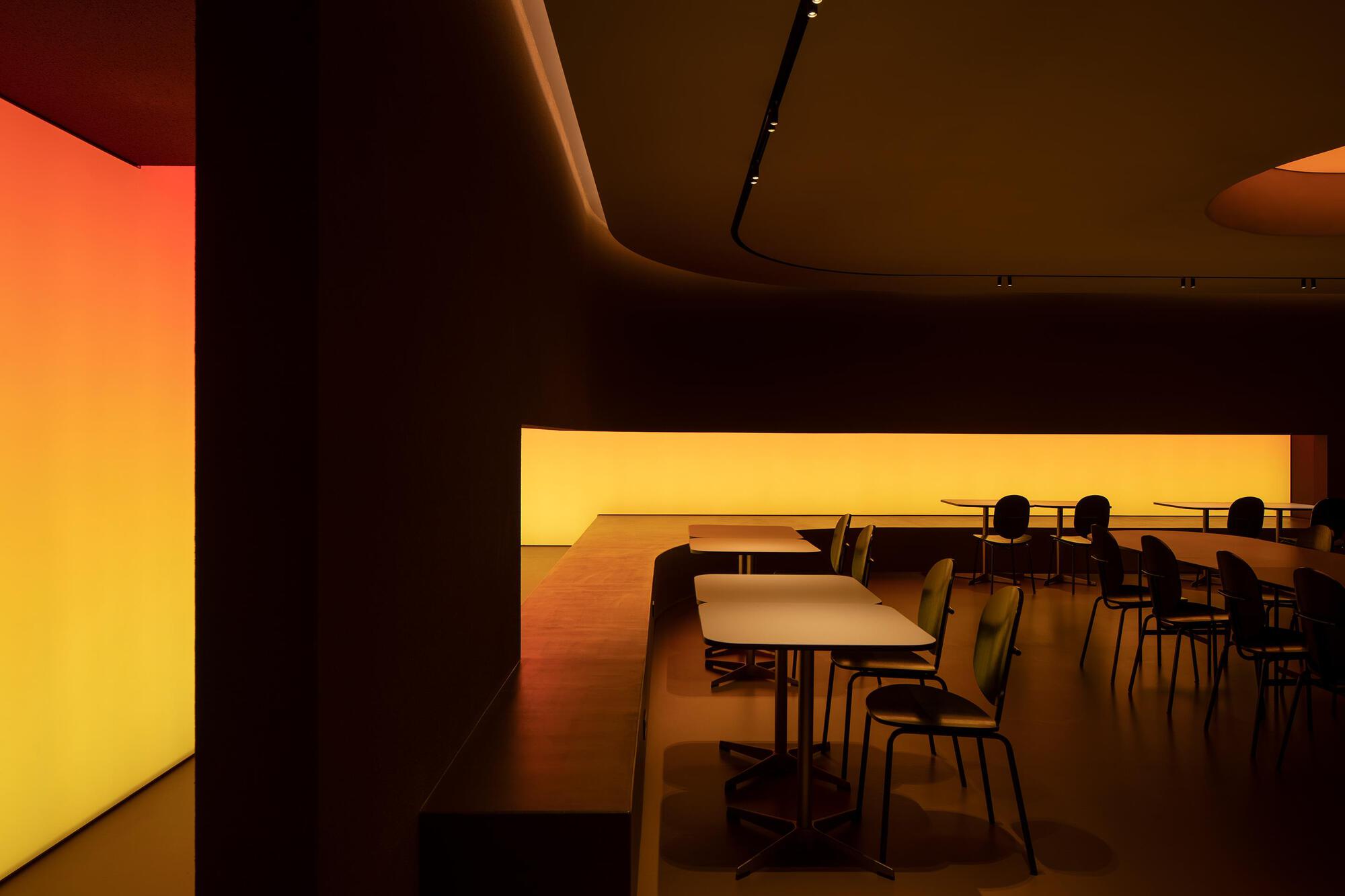 Cafe tables and chairs beneath curved ceiling with backlit amber wall panels