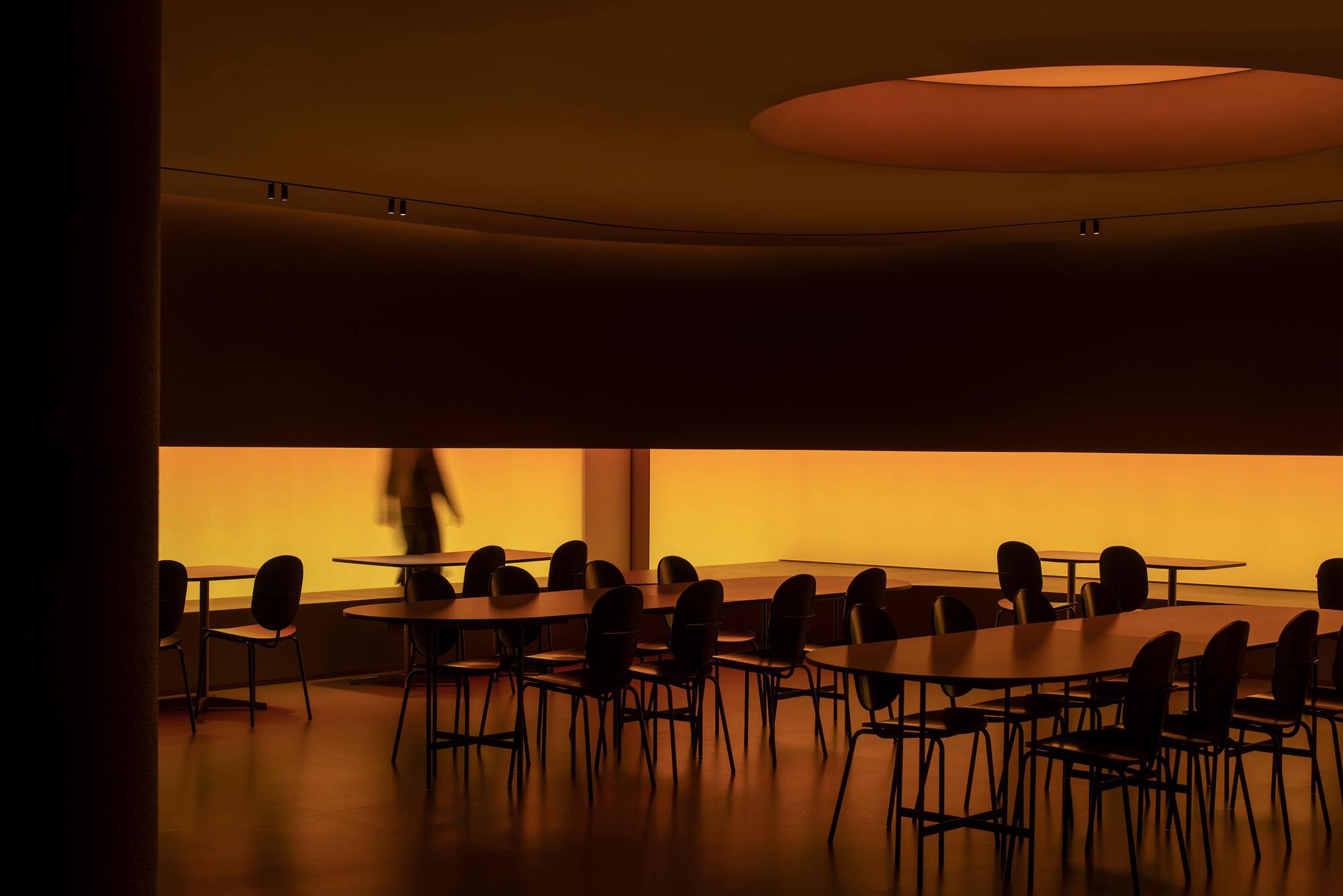 Dining area with curved ceiling oculus and backlit amber translucent wall panel with a figure passing