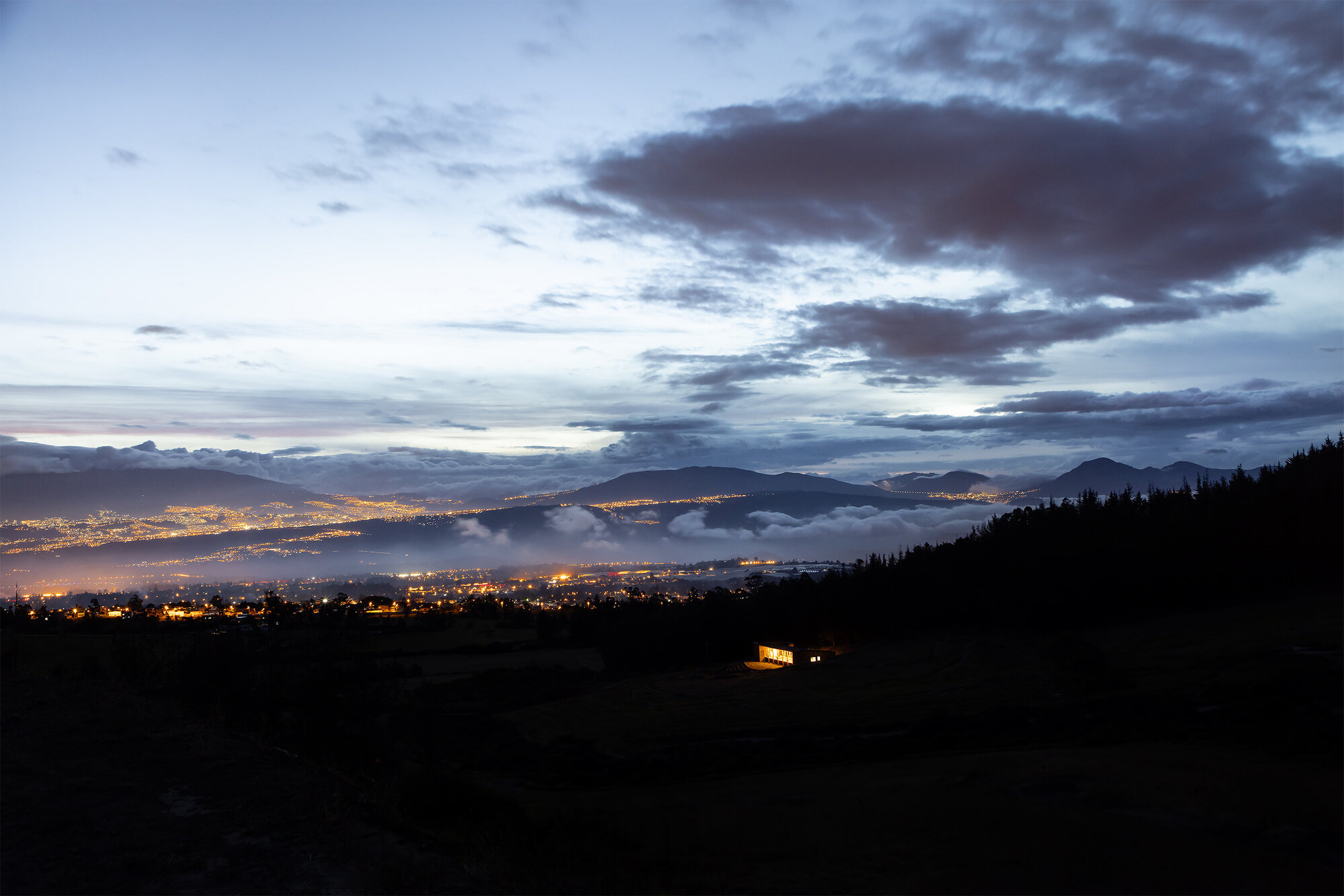 Distant view of the illuminated building on a dark slope above a lit valley at dusk