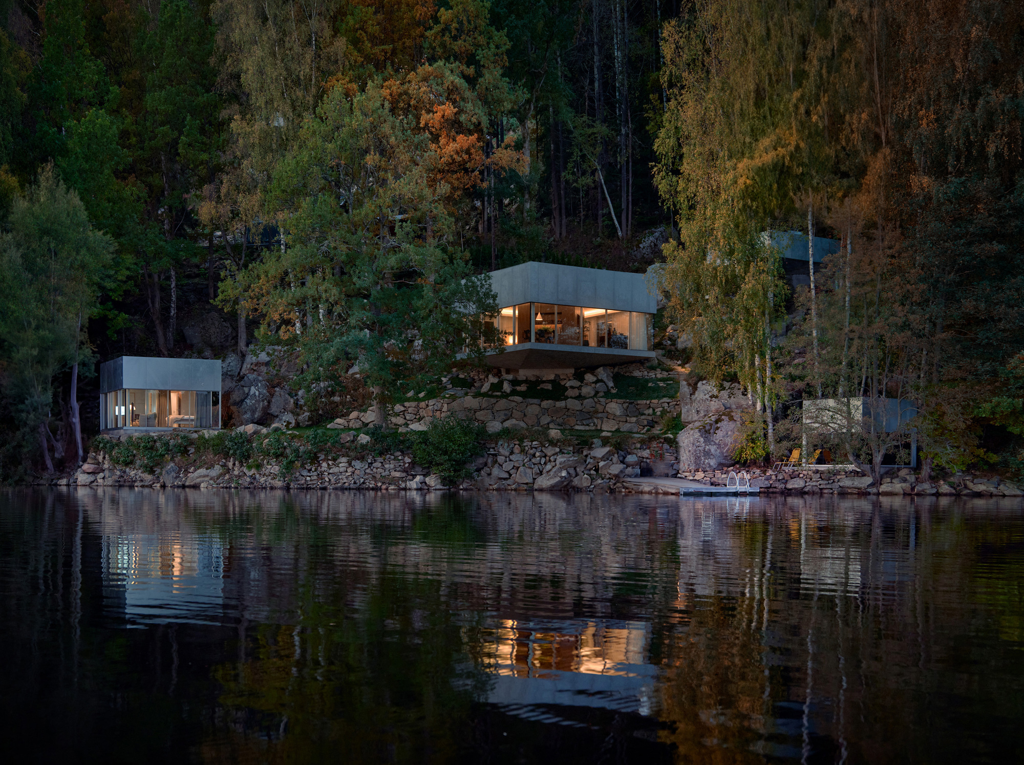 Three pavilions on a rocky lakeside slope illuminated at dusk with reflections in the still water