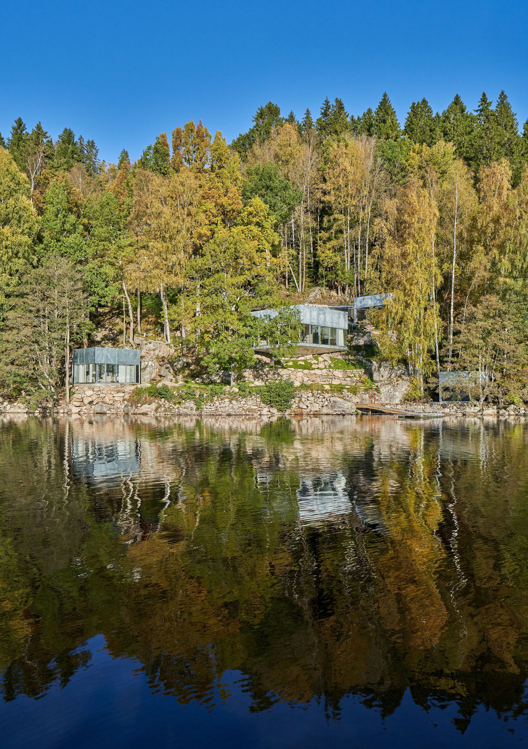 Three glass pavilions nestled among boulders and autumn trees reflected in the calm lake surface